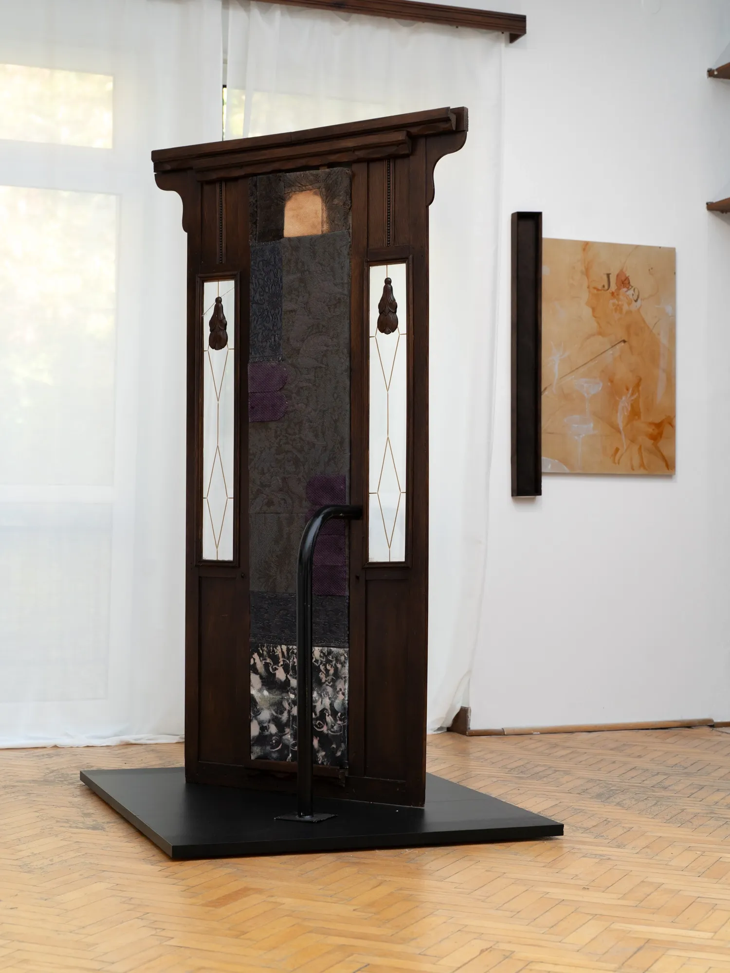 Cyprian Szablak, MISE EN, Warsaw: dark wooden door-like structure with leaded glass panes and a black rail, an orange canvas behind.