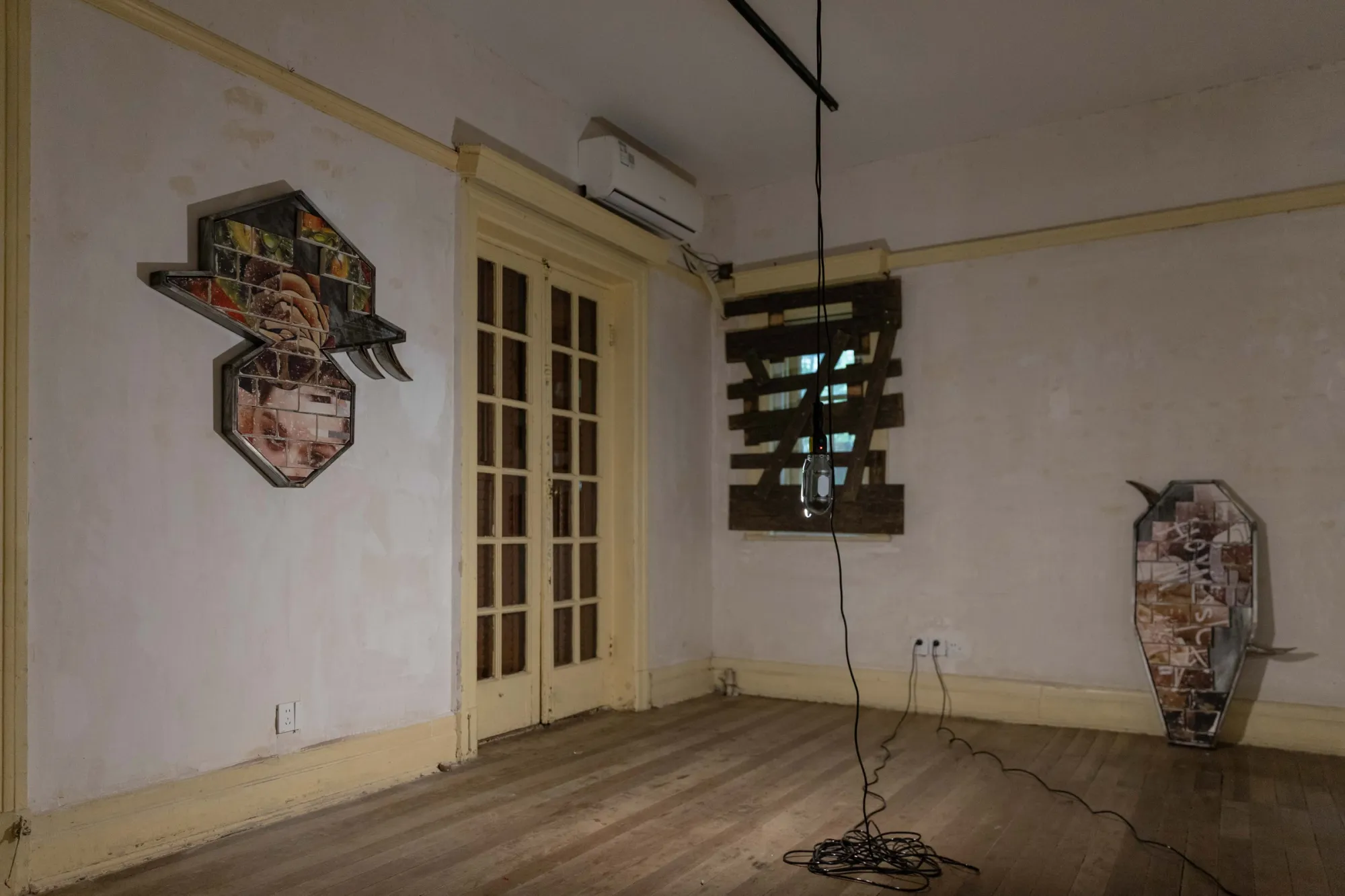 Fangyang, E.SCAPE art space, Shanghai: hat-shaped wall work and an upright coffin-shaped work in a room with boarded windows and a hanging bulb.