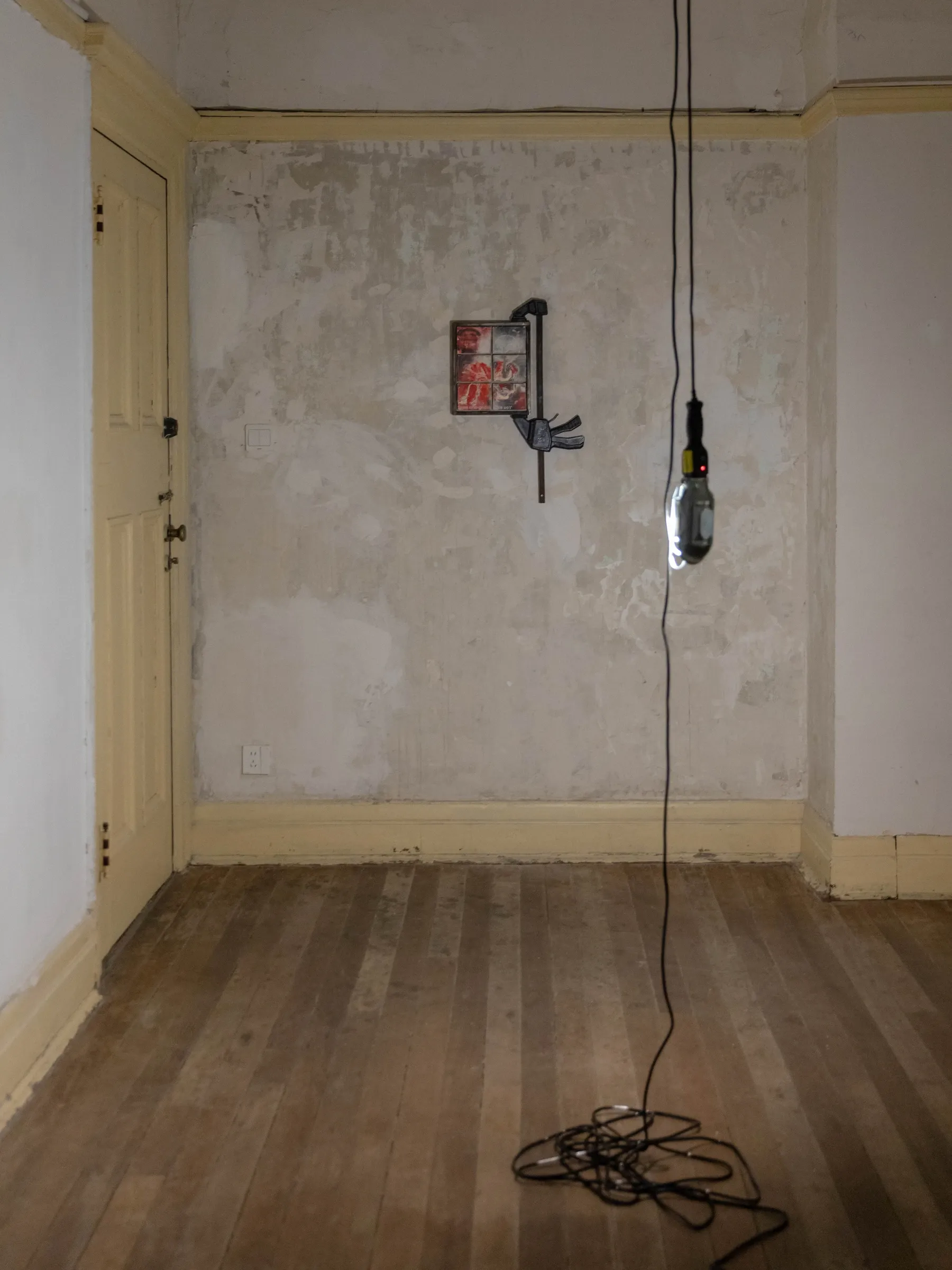 Fangyang, E.SCAPE art space, Shanghai: empty room with a small clamp-mounted work on a worn plaster wall and a coiled cable below a hanging bulb.