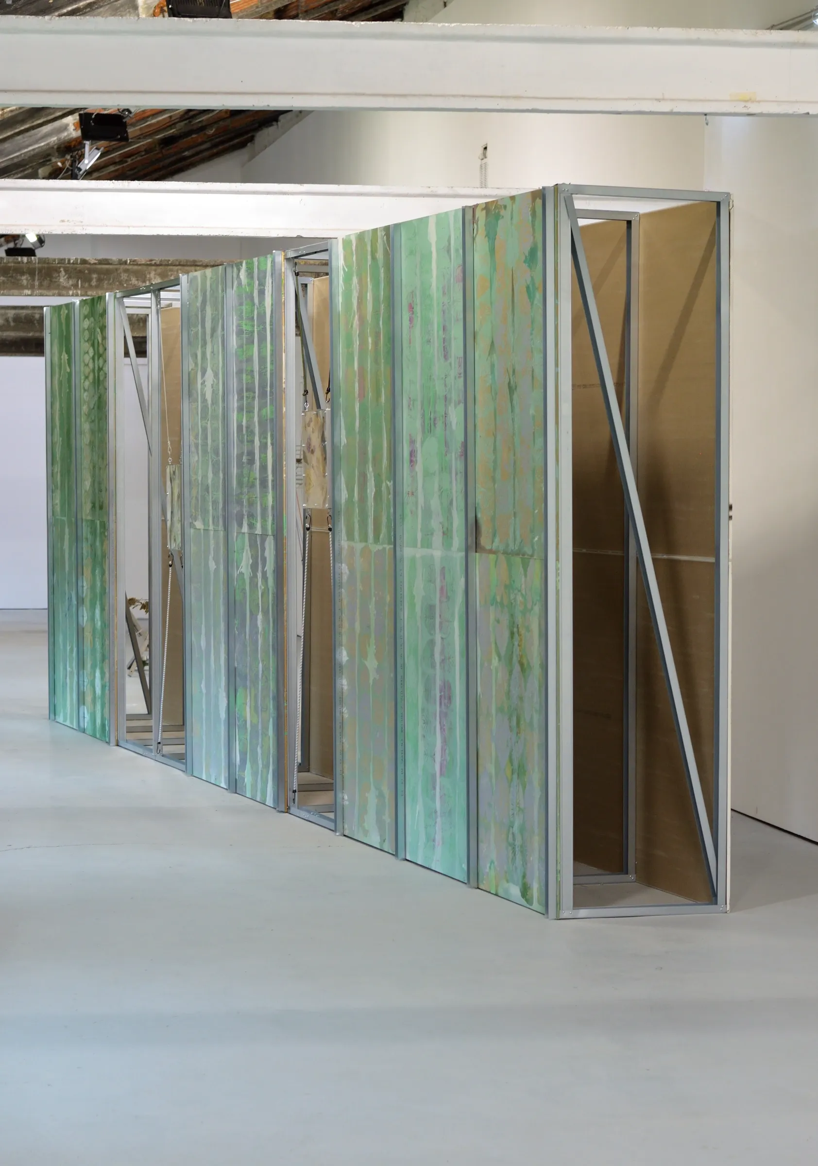 Exhibition review of Gabriel Alonso: A Long Chemical Dream at ATM Galería, Gijón, 2026. Freestanding wall of green printed panels in an aluminium frame.