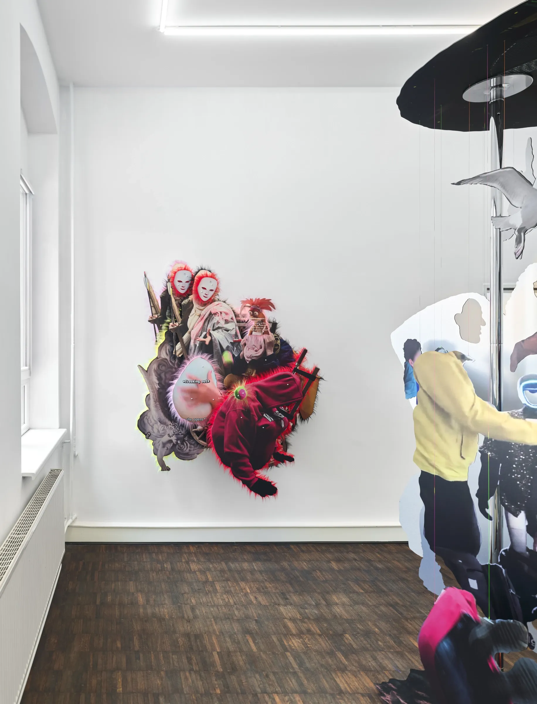 Exhibition review of Iris Helena Hamers: ~^-.3N3RGY_4NG3L.-^~ at PAW, Düsseldorf, 2026. Wall work of masked faces and a red hooded figure beside the lower part of the dance pole sculpture, parquet floor.