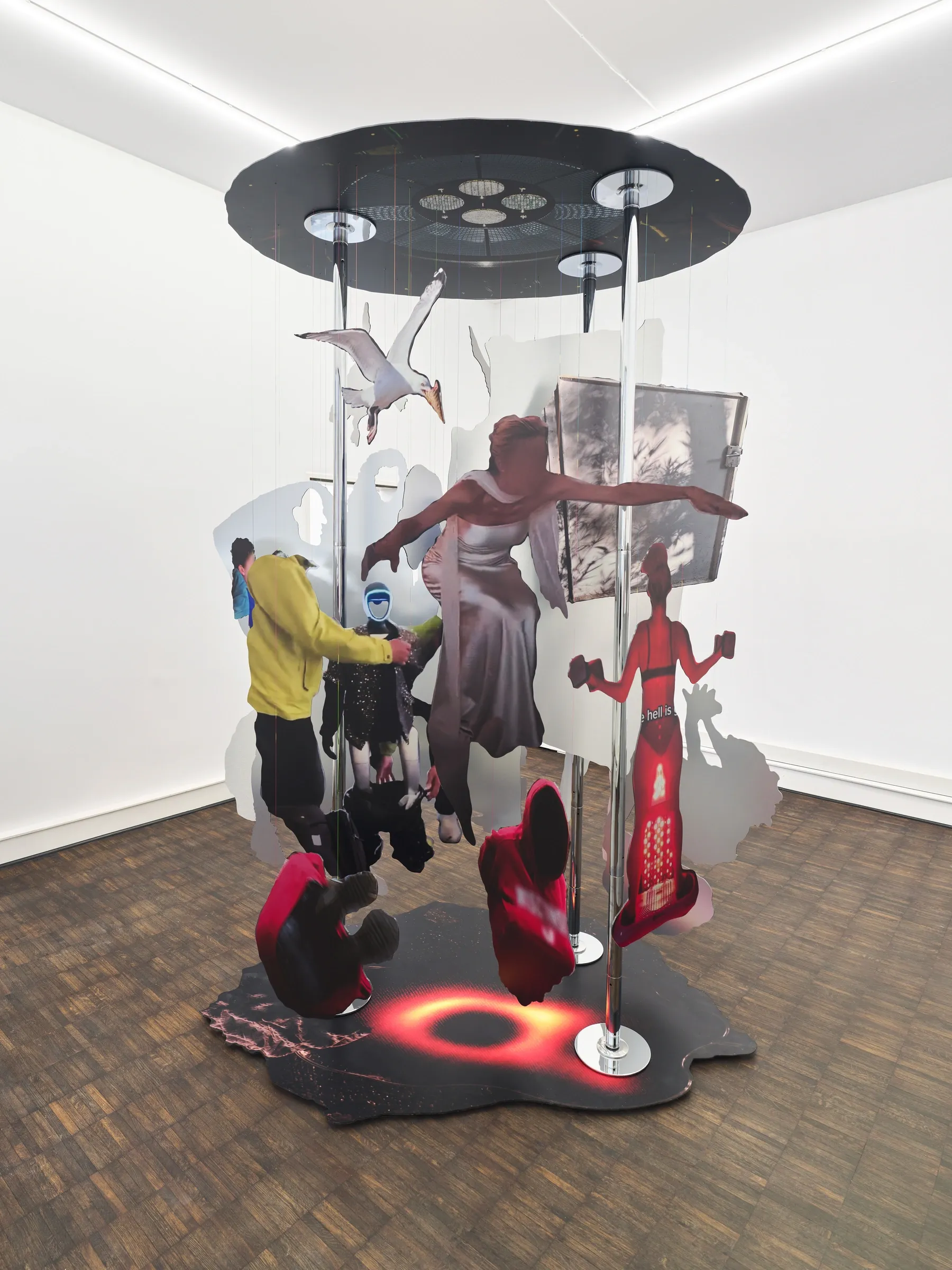Exhibition review of Iris Helena Hamers: ~^-.3N3RGY_4NG3L.-^~ at PAW, Düsseldorf, 2026. Dance pole sculpture from another side, with a yellow jacketed figure, a figure in red and a glowing red ring on the floor.