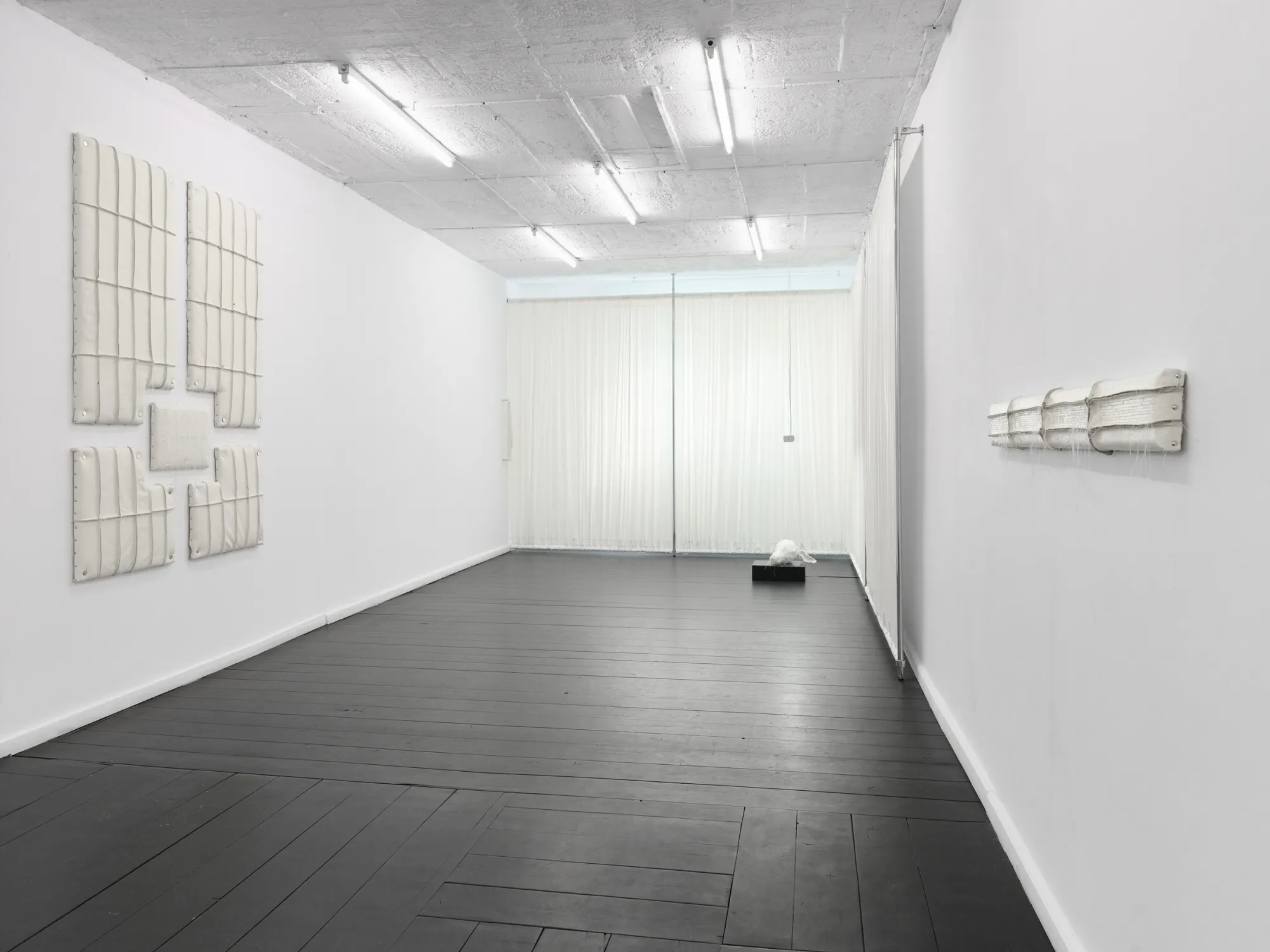 Long gallery with cream padded wall panels, sheer curtains and a distant deer sculpture. Jan Baszak, Within and For Each Other, WHOISPOLA, Warsaw, 2026.