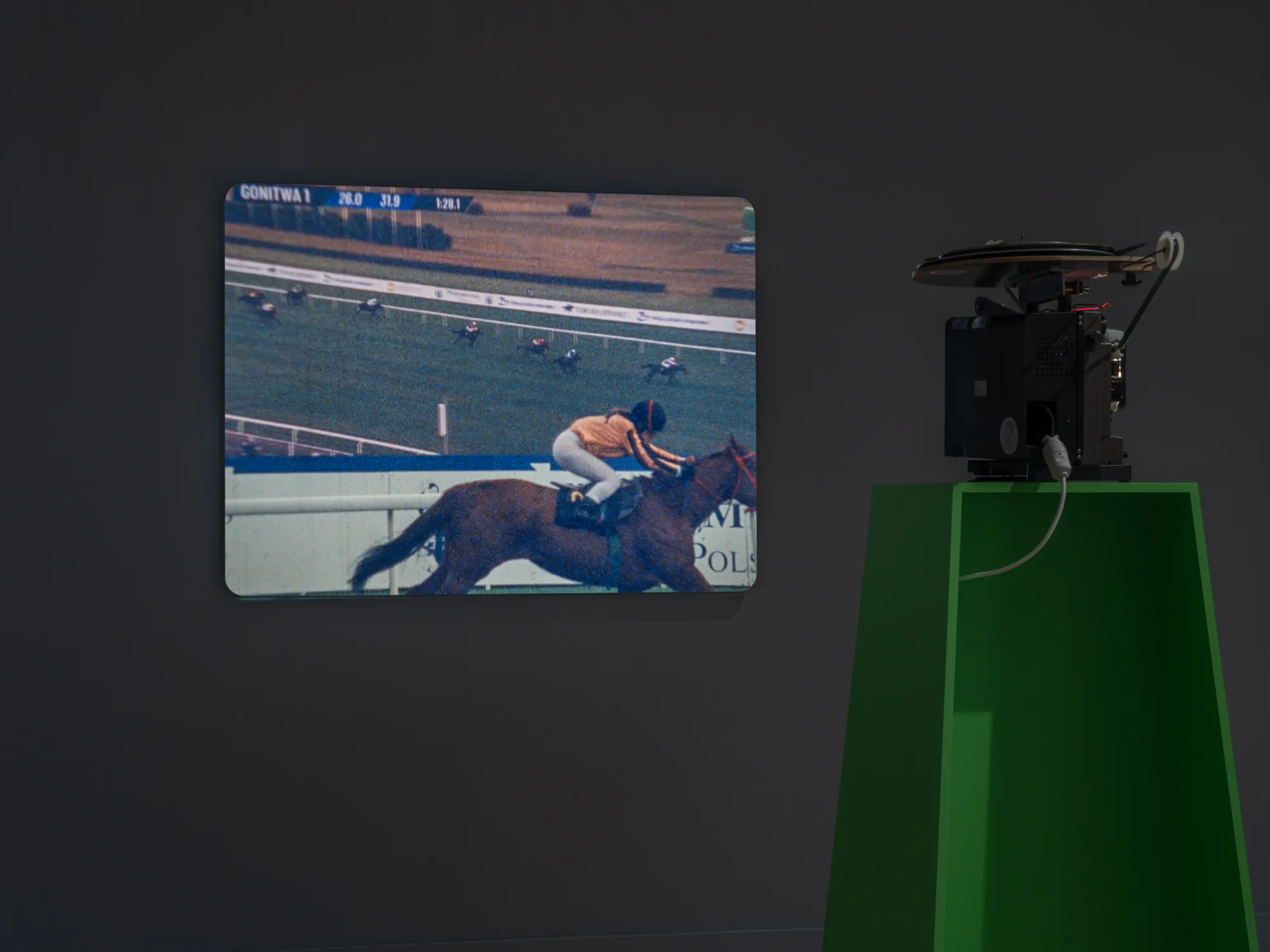 João Maria Gusmão, Zachęta, Warsaw: projected jockey on a horse at a racecourse beside a green plinth with a 16mm projector.