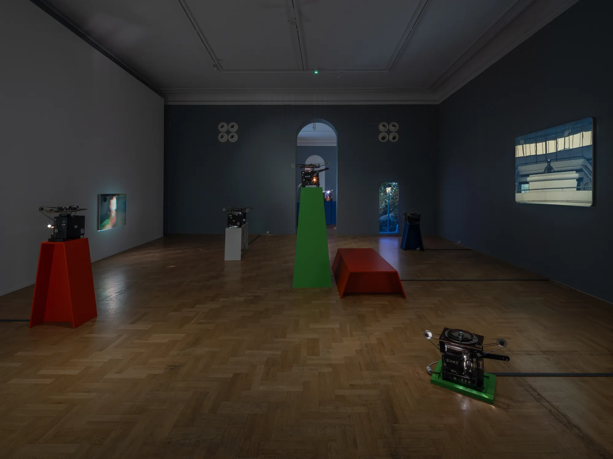 ALT: João Maria Gusmão, Zachęta, Warsaw: dark gallery with parquet floor, red and green projector plinths and film projections on grey walls.