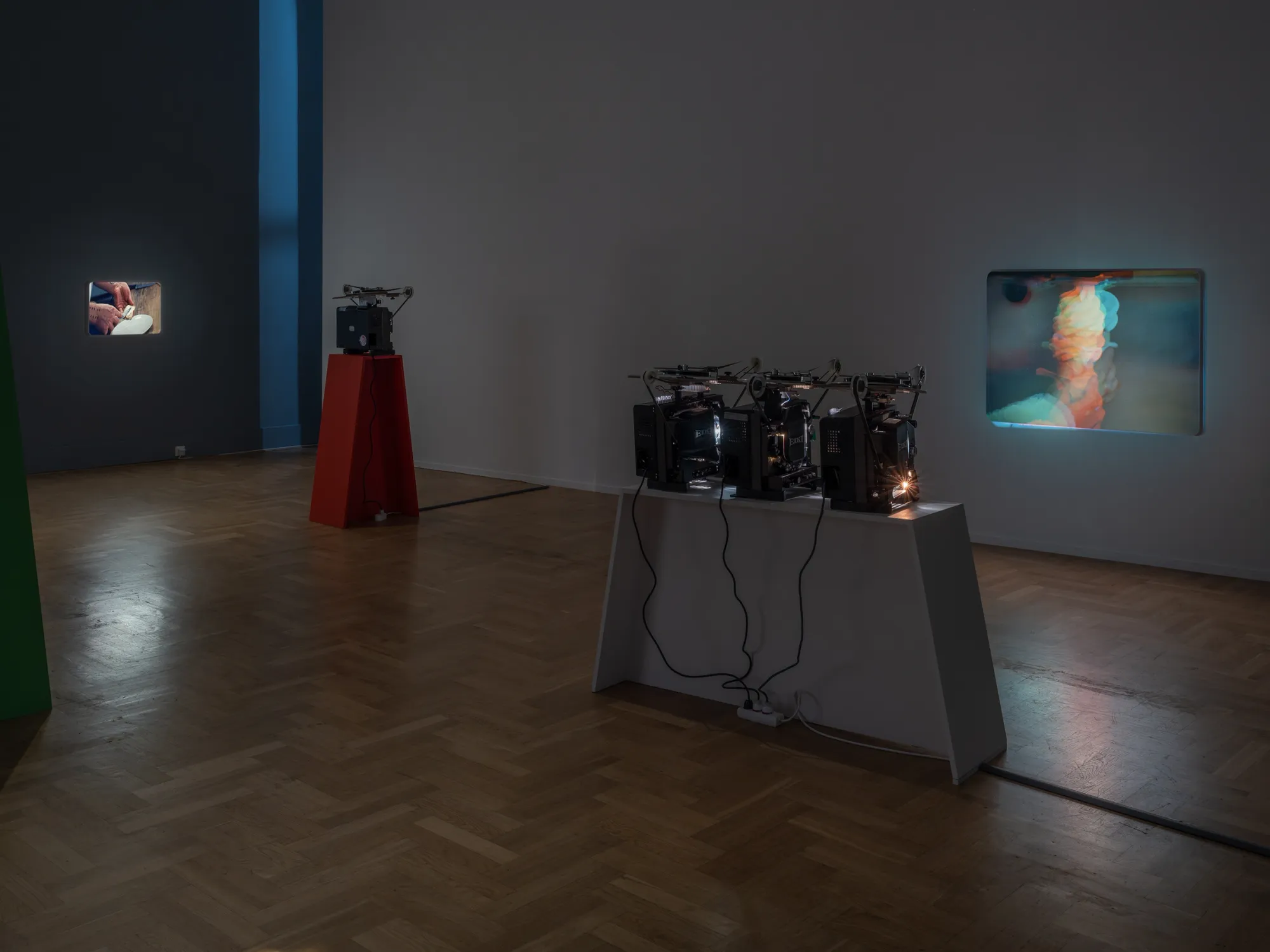 João Maria Gusmão, Zachęta, Warsaw: three 16mm projectors on a white plinth facing a colour-split wall projection, small bread projection at left.