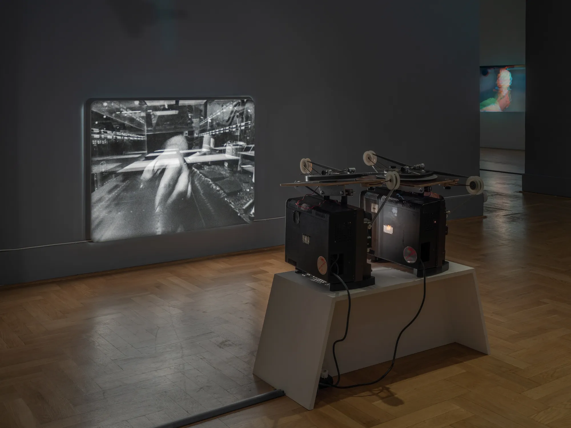 João Maria Gusmão, Zachęta, Warsaw: black-and-white projection of a factory hall with a blurred hand, two projectors on a white plinth.