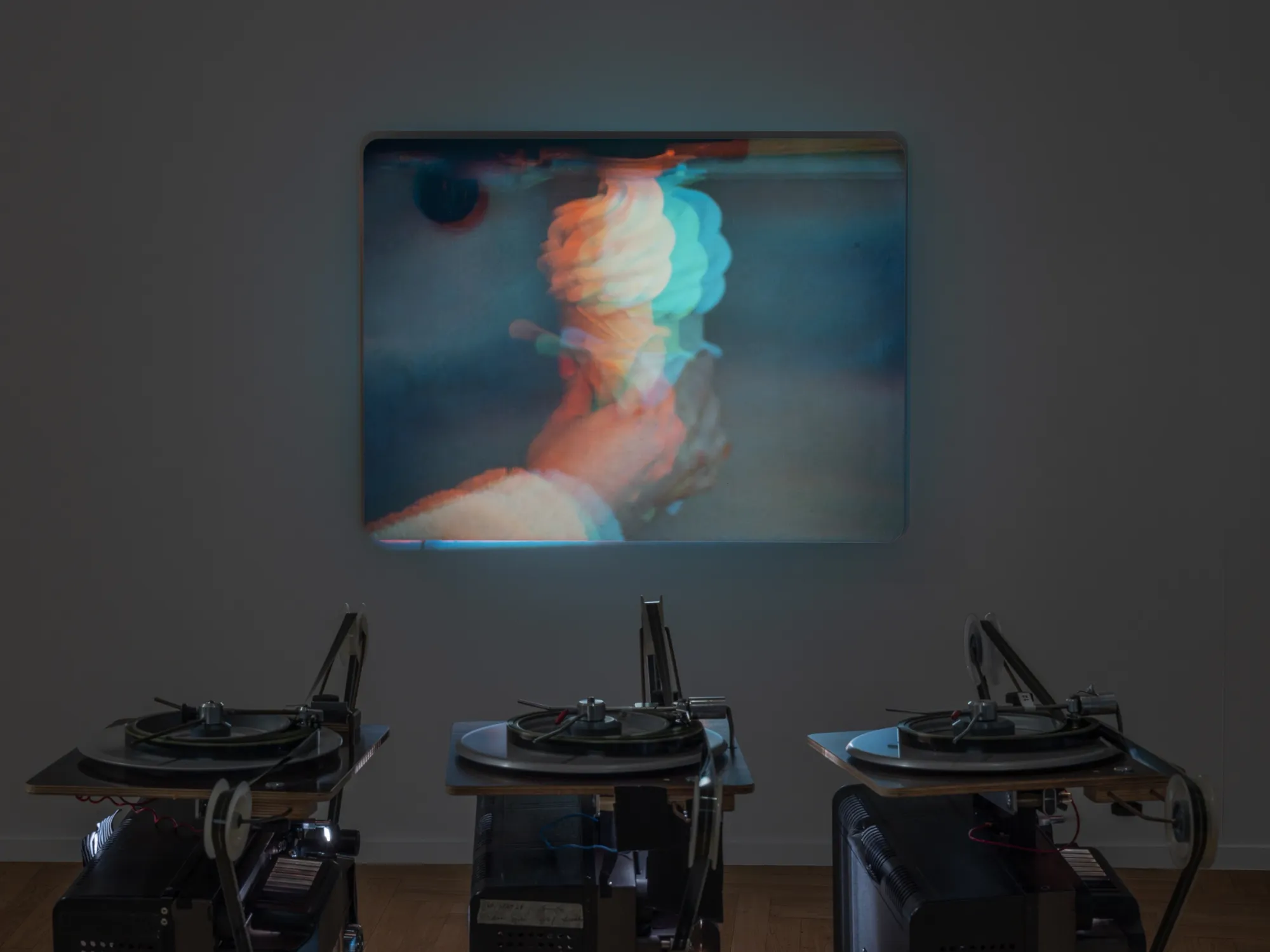 ALT: João Maria Gusmão, Zachęta, Warsaw: wall projection of a hand and a pale swirled form in cyan and orange fringes above three film reels.