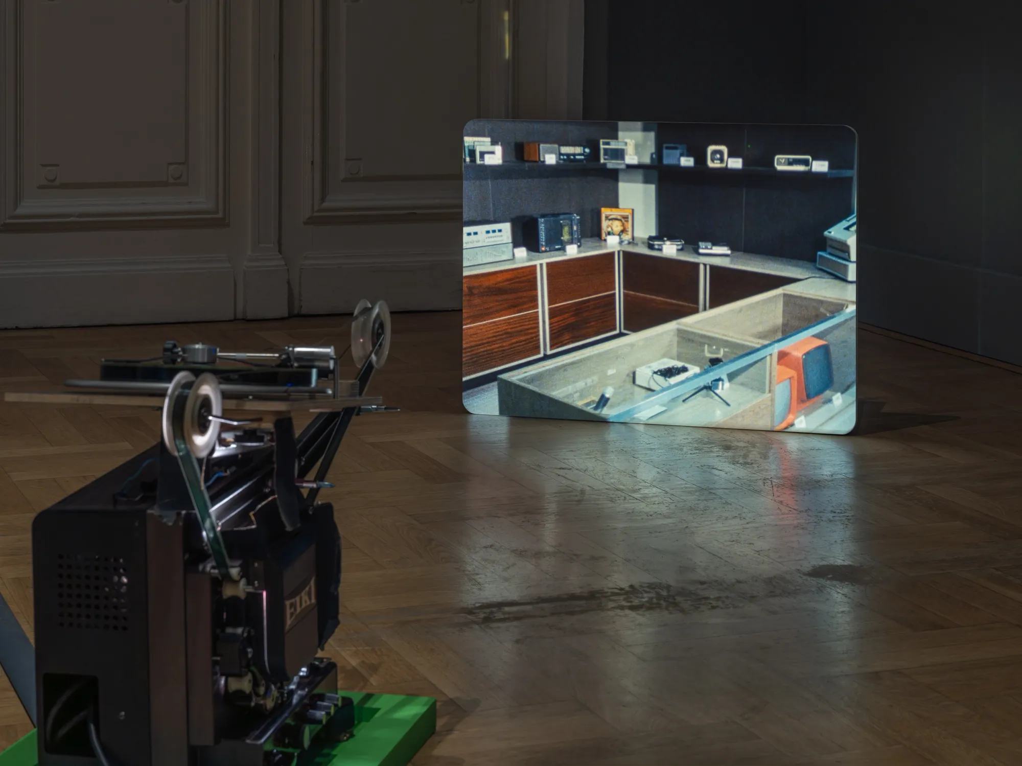 ALT: João Maria Gusmão, Zachęta, Warsaw: projected interior of a retro electronics shop with a 16mm projector on a green base on the parquet floor.