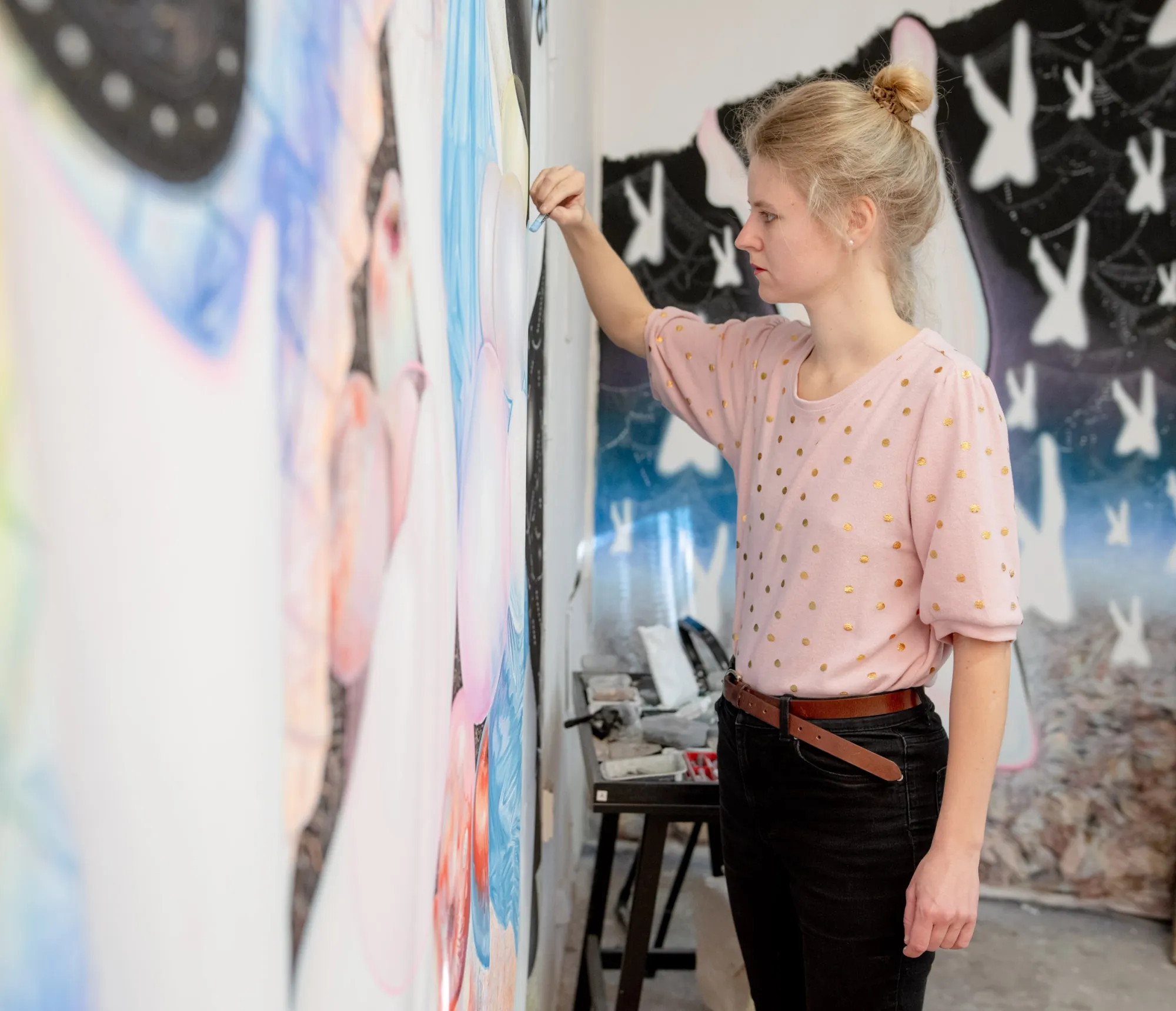 Karolína Netolická, Prague: the artist works on a large pastel canvas in her studio, beside a trolley of materials.