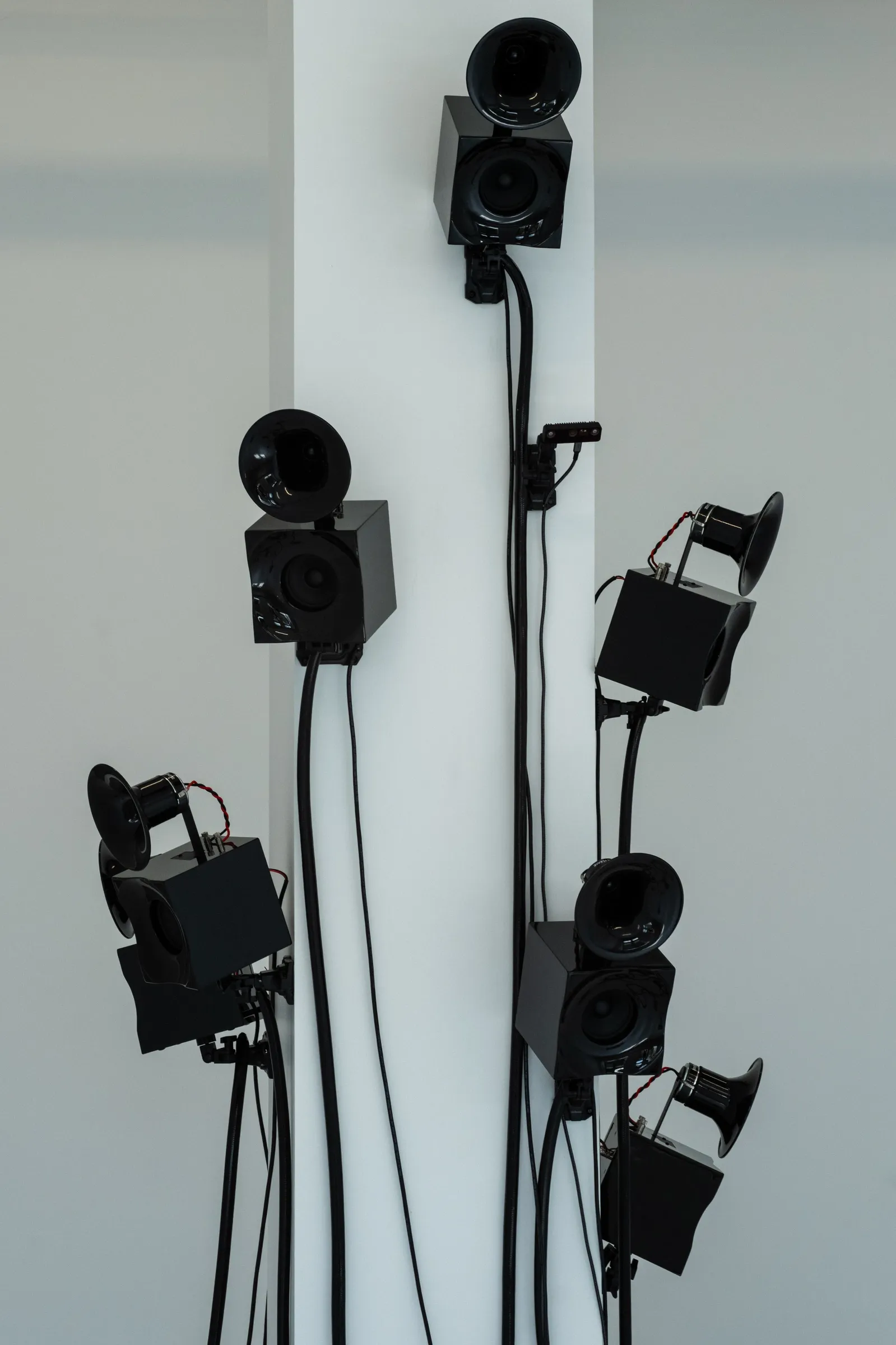 Artist Profile Feature: KiefferWoodtli, Arboreal Severance, New York, 2025. Black speakers at different heights on a white column, cables hanging down.