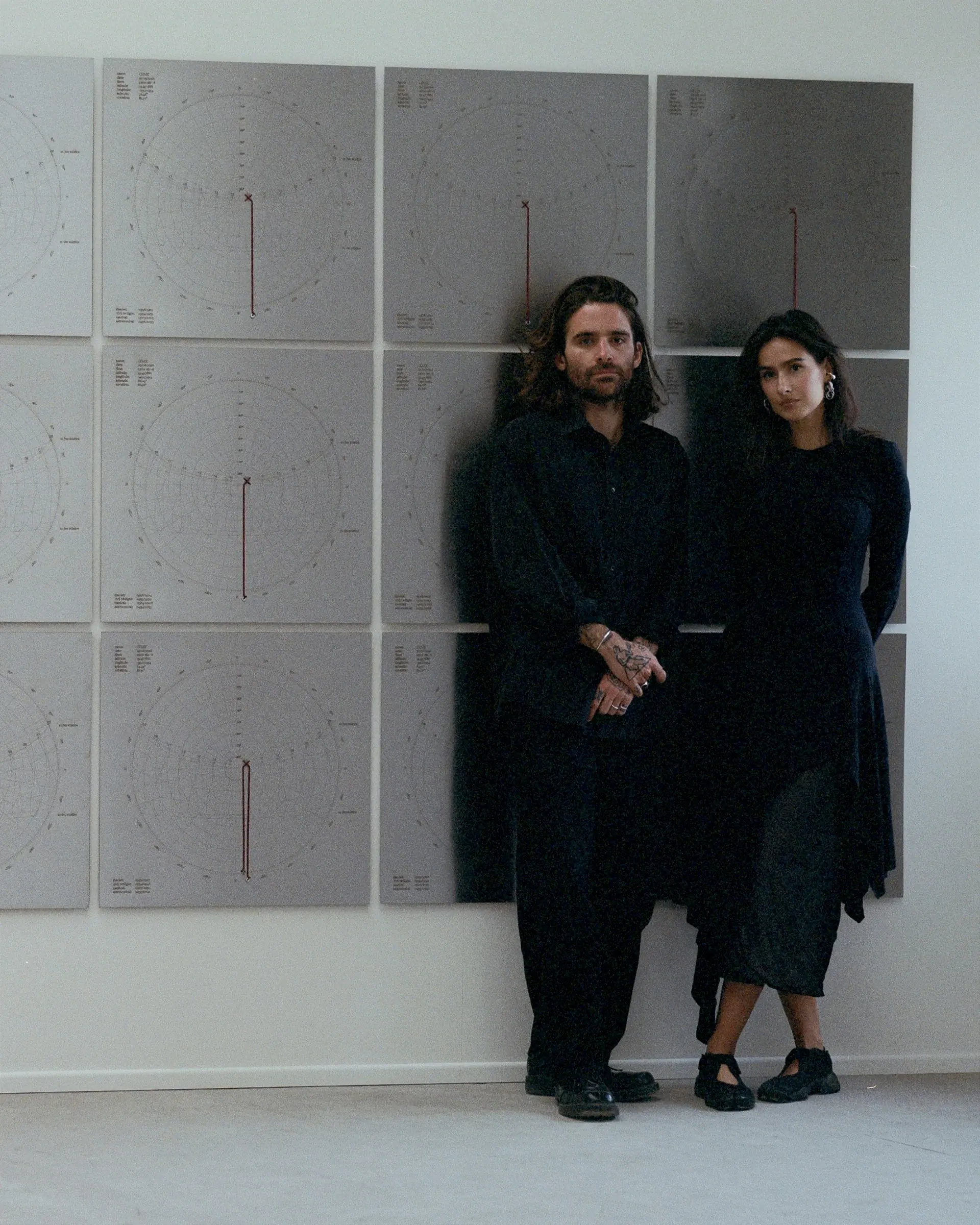 Artist Profile Feature: KiefferWoodtli, portrait of the artist duo. Two people in black stand before a wall of grey solar chart panels.