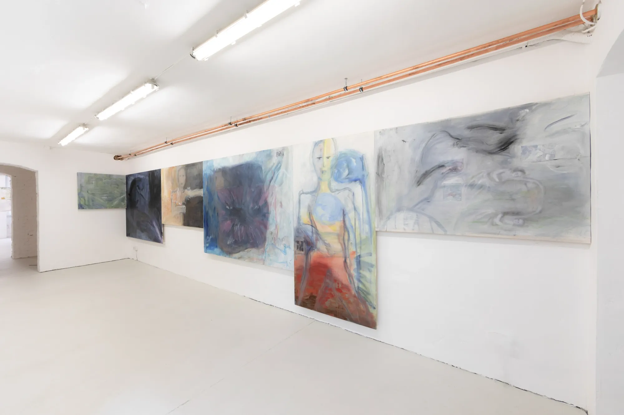 Exhibition review of Krys Huba: falling into you at soft power, Berlin, 2026. Long white wall with six overlapping oil paintings under copper pipes.