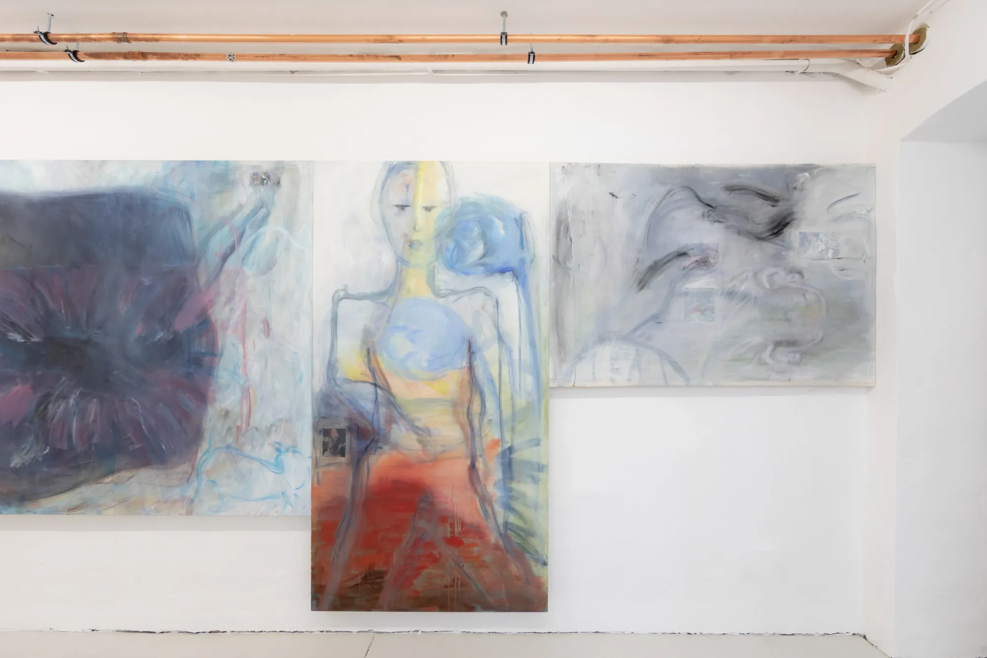 Exhibition review of Krys Huba: falling into you at soft power, Berlin, 2026. Standing figure in red and blue between a flower painting and grey canvas.