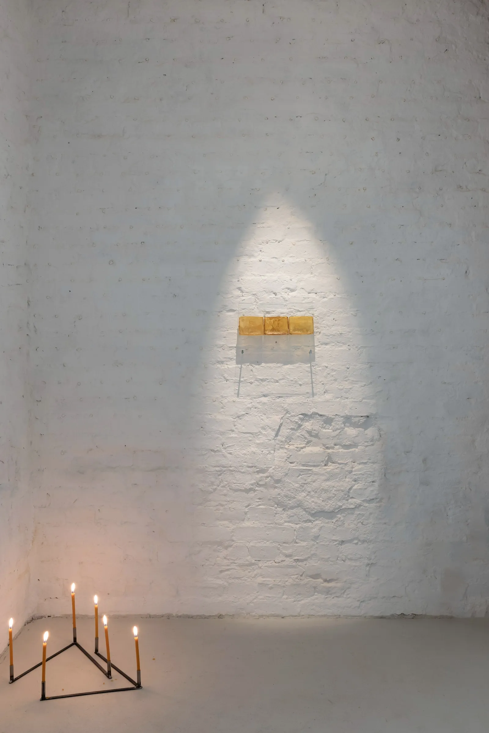 Exhibition review of Krys Huba: falling into you at soft power, Berlin, 2026. Amber latex panels in a spotlight on brick, lit candles on the floor.