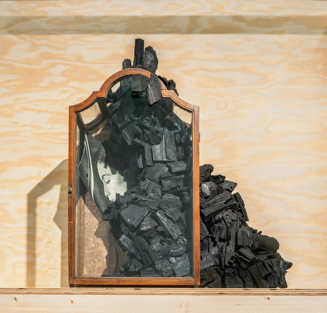 Lucia Tallová, Moving Clouds, PalaisPopulaire, Berlin. Wooden glass-fronted cabinet containing a woman's image and piled black material.