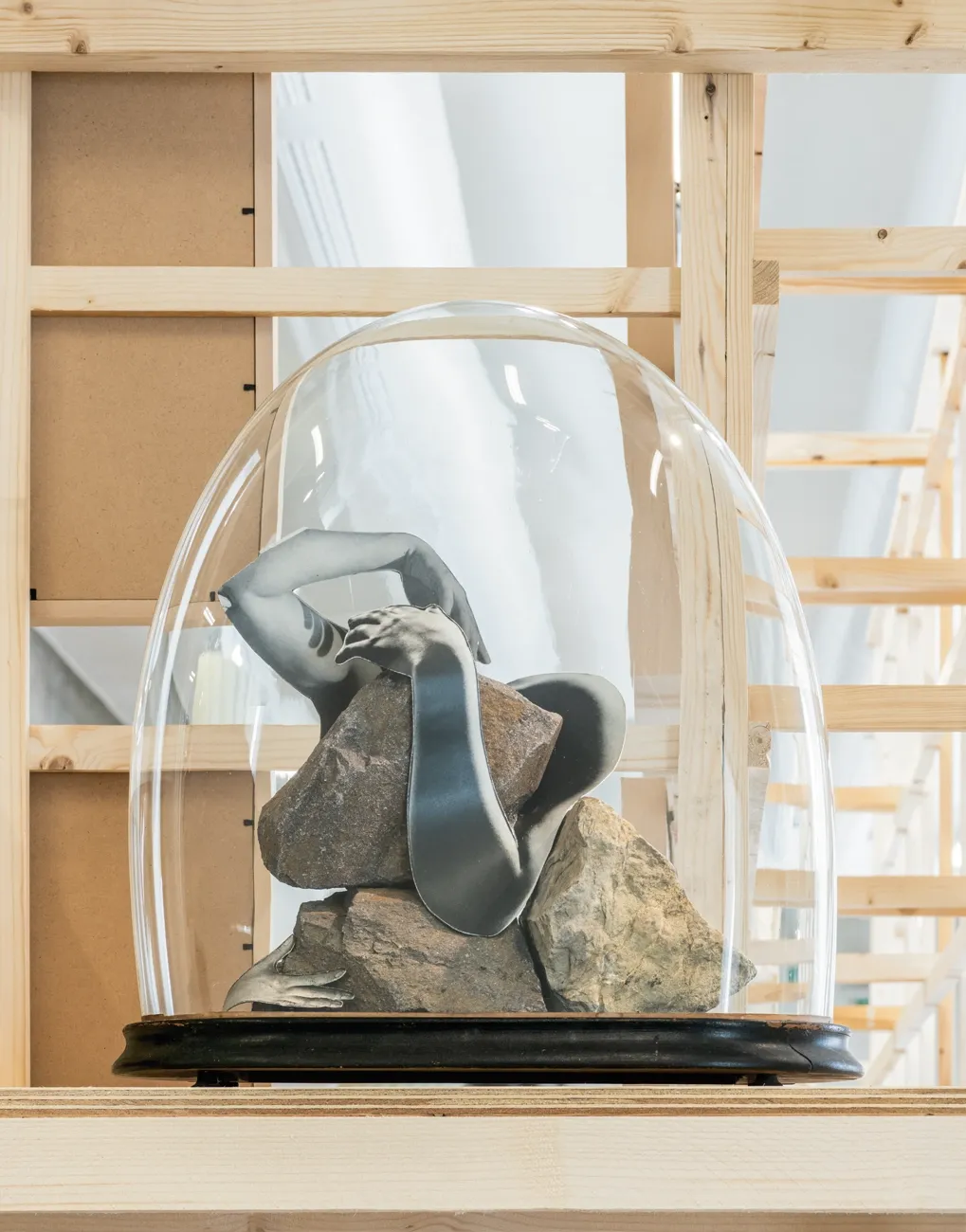 Lucia Tallová, PalaisPopulaire, Berlin: glass dome on a black base covering stones and a cut-out printed arm in grey tones.