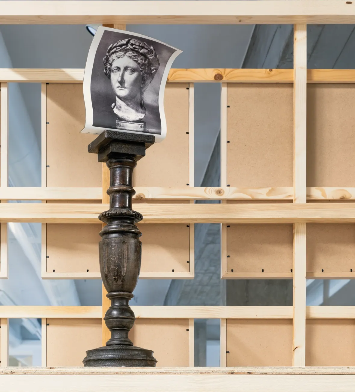 Lucia Tallová, PalaisPopulaire, Berlin: cut-out printed photograph of a laurel-crowned bust bent over a dark turned wooden pedestal.