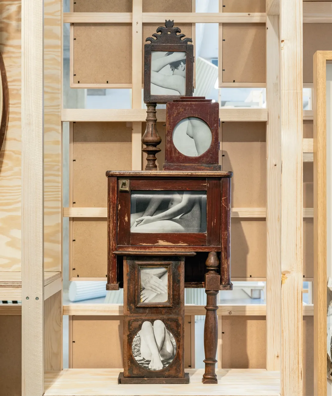 Lucia Tallová, PalaisPopulaire, Berlin: stacked dark wooden cabinet parts holding photographs of crossed arms and legs behind glass.