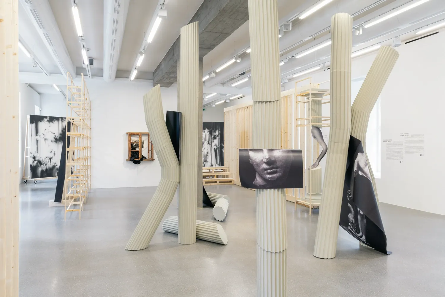 Lucia Tallová, PalaisPopulaire, Berlin: bent pale green fluted columns with printed female torso images in a white gallery room.