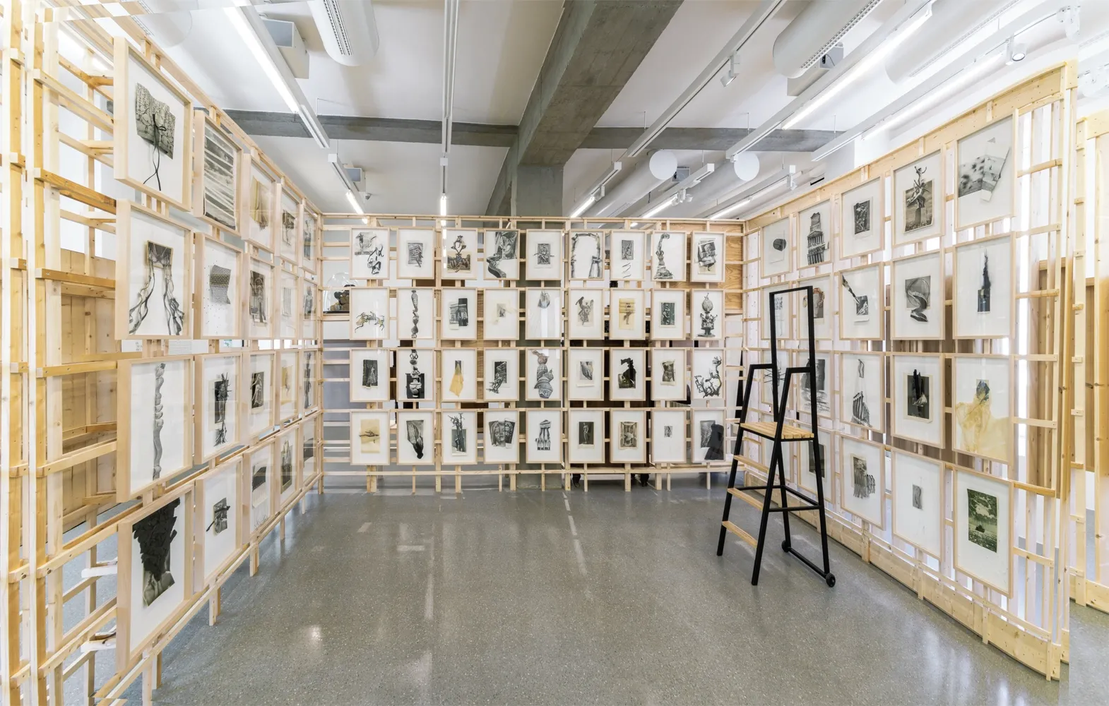 Lucia Tallová, PalaisPopulaire, Berlin: room lined with wooden lattice walls holding dense rows of framed collages and a black stepladder.