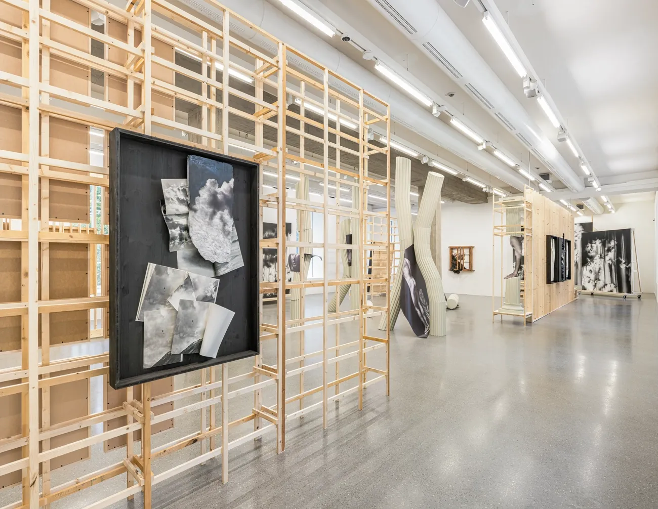 Lucia Tallová, PalaisPopulaire, Berlin: hall with timber lattice walls, bent green columns and a framed cloud collage in the foreground.