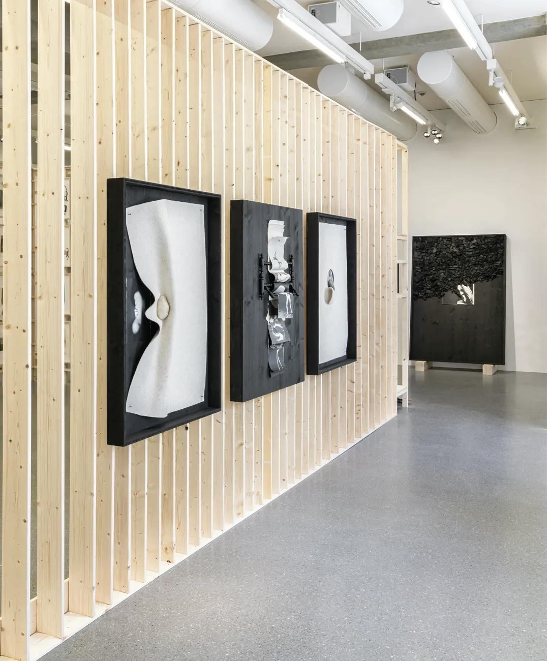 Lucia Tallová, PalaisPopulaire, Berlin: three black-framed works with cream fabric, layered paper and stones on a slatted timber wall.