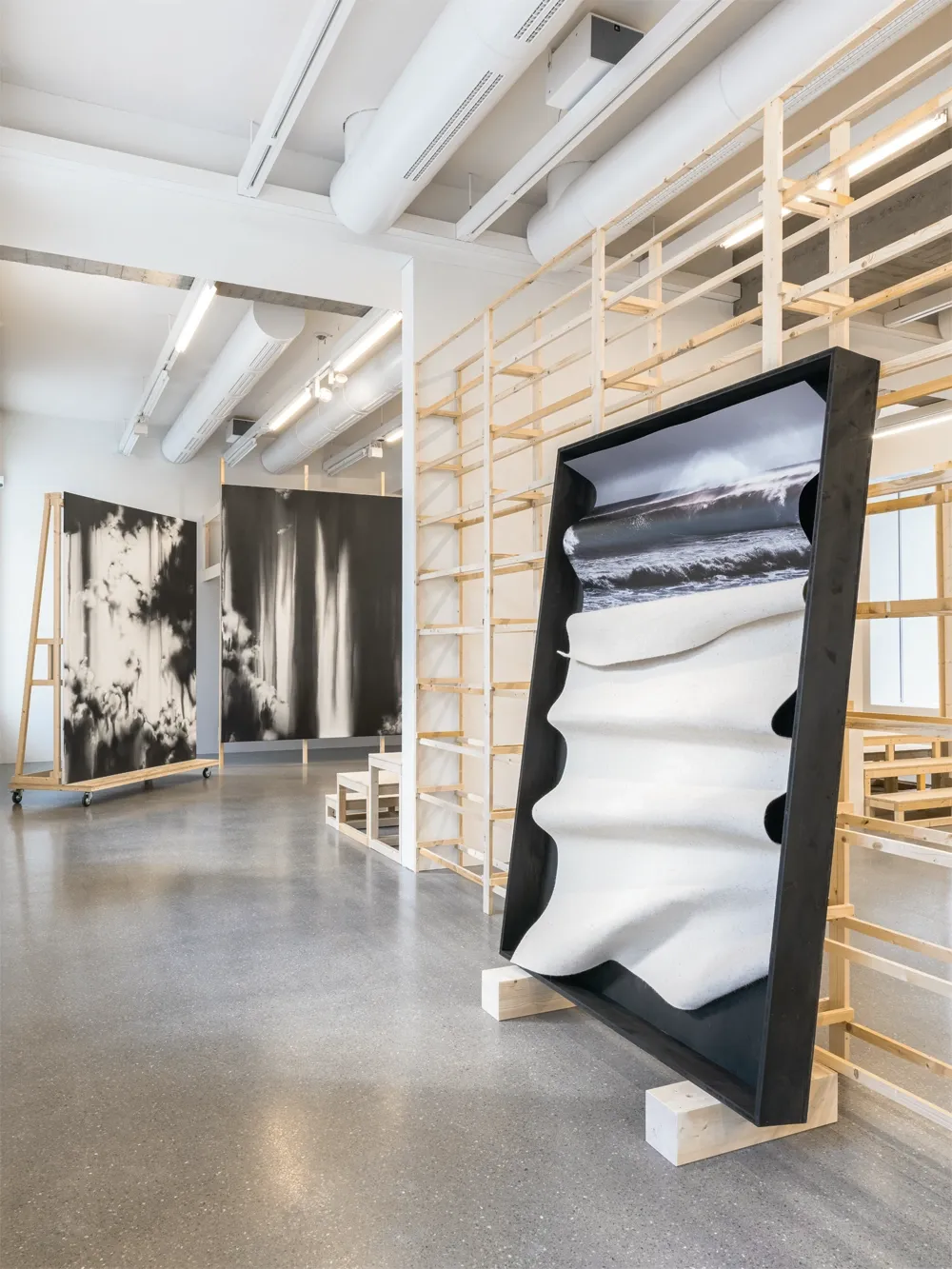 Lucia Tallová, PalaisPopulaire, Berlin: pleated cream fabric below a wave photograph in a black frame on timber blocks.