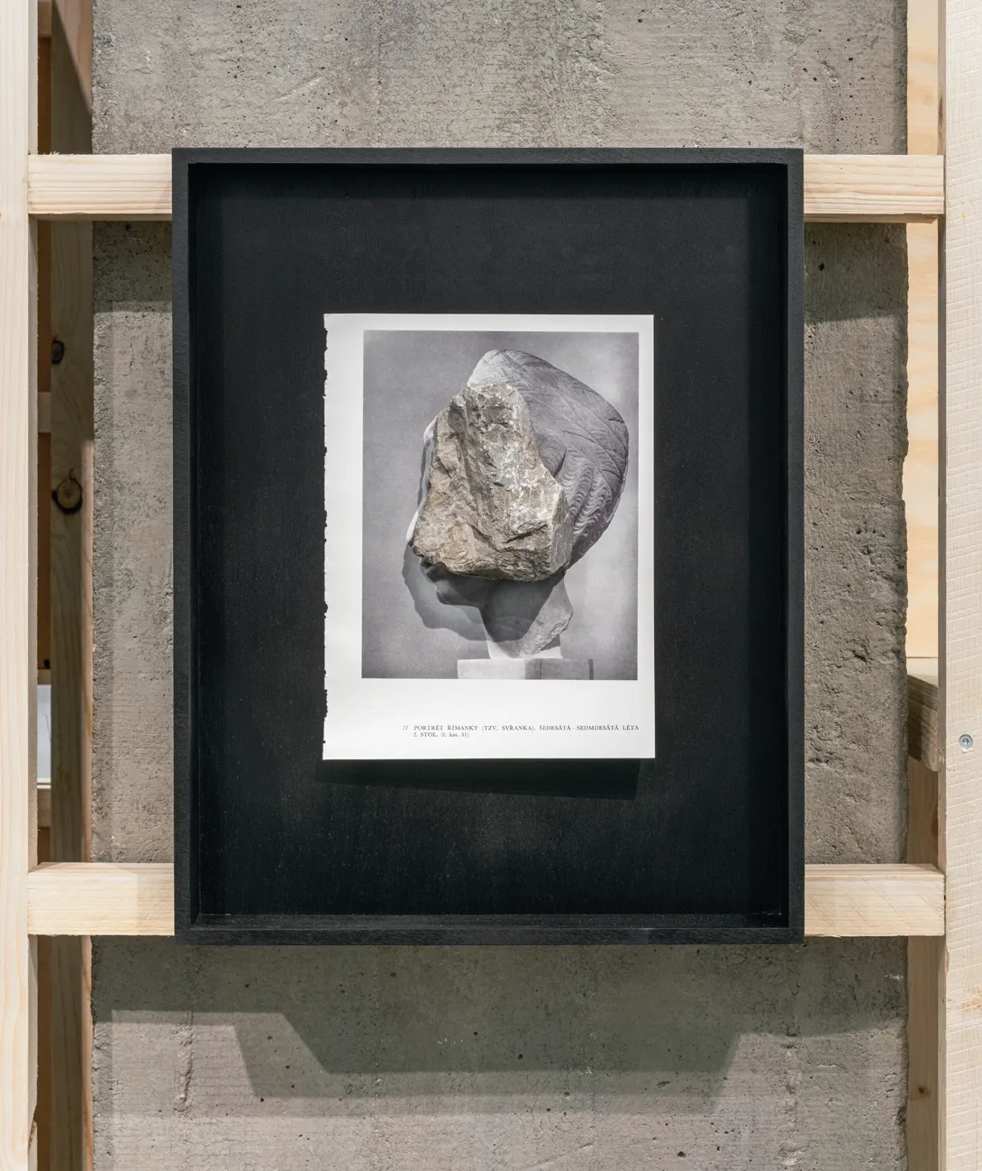 Lucia Tallová, PalaisPopulaire, Berlin: black frame with a book page showing a stone laid over a sculpted head.
