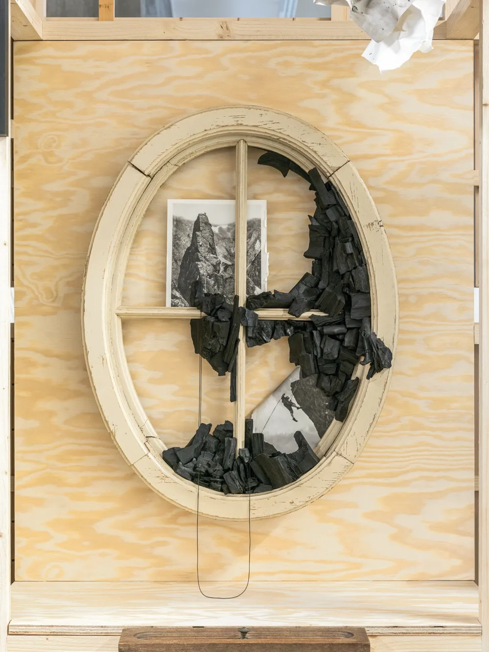 Lucia Tallová, PalaisPopulaire, Berlin: oval cream window frame filled with charcoal pieces and a mountain photograph.