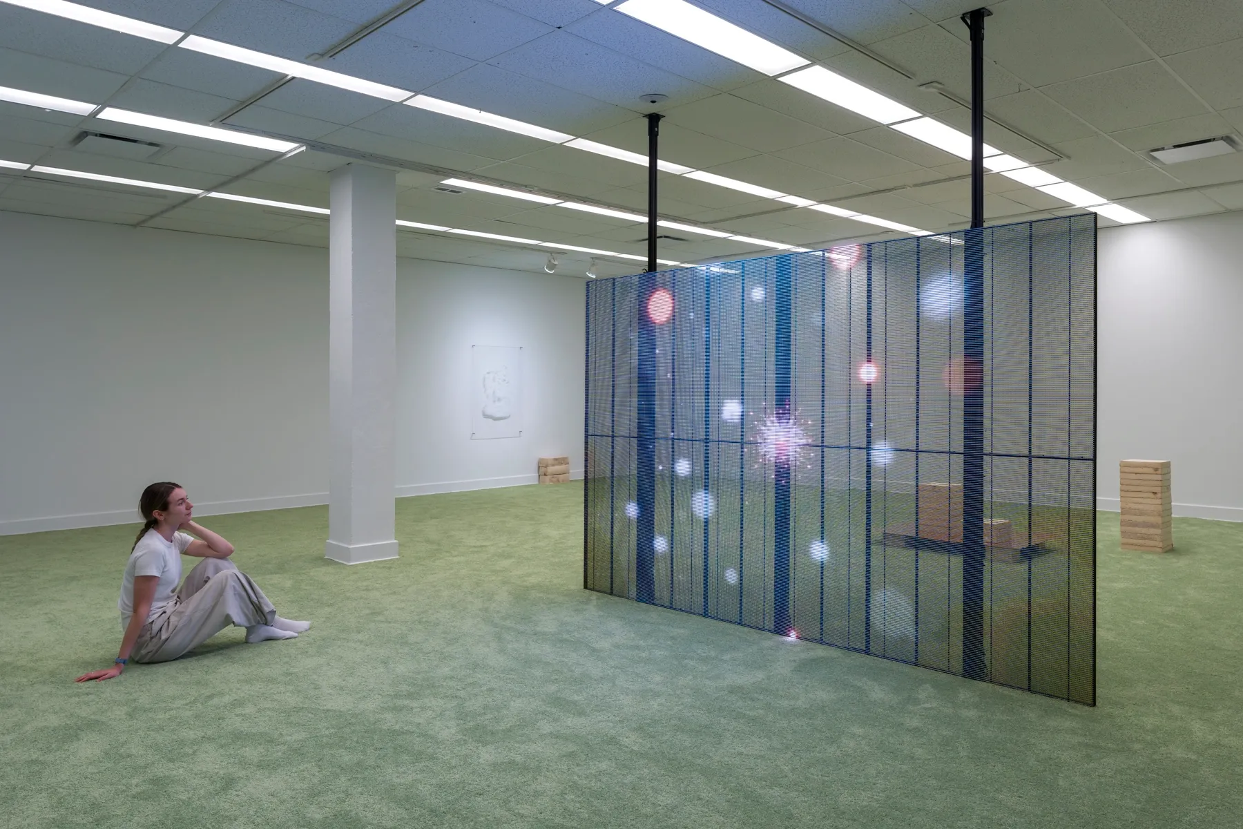 Visitor seated on green carpet facing Patrick Bérubé’s LED installation with blue grids and blurred lights at Plein Sud.