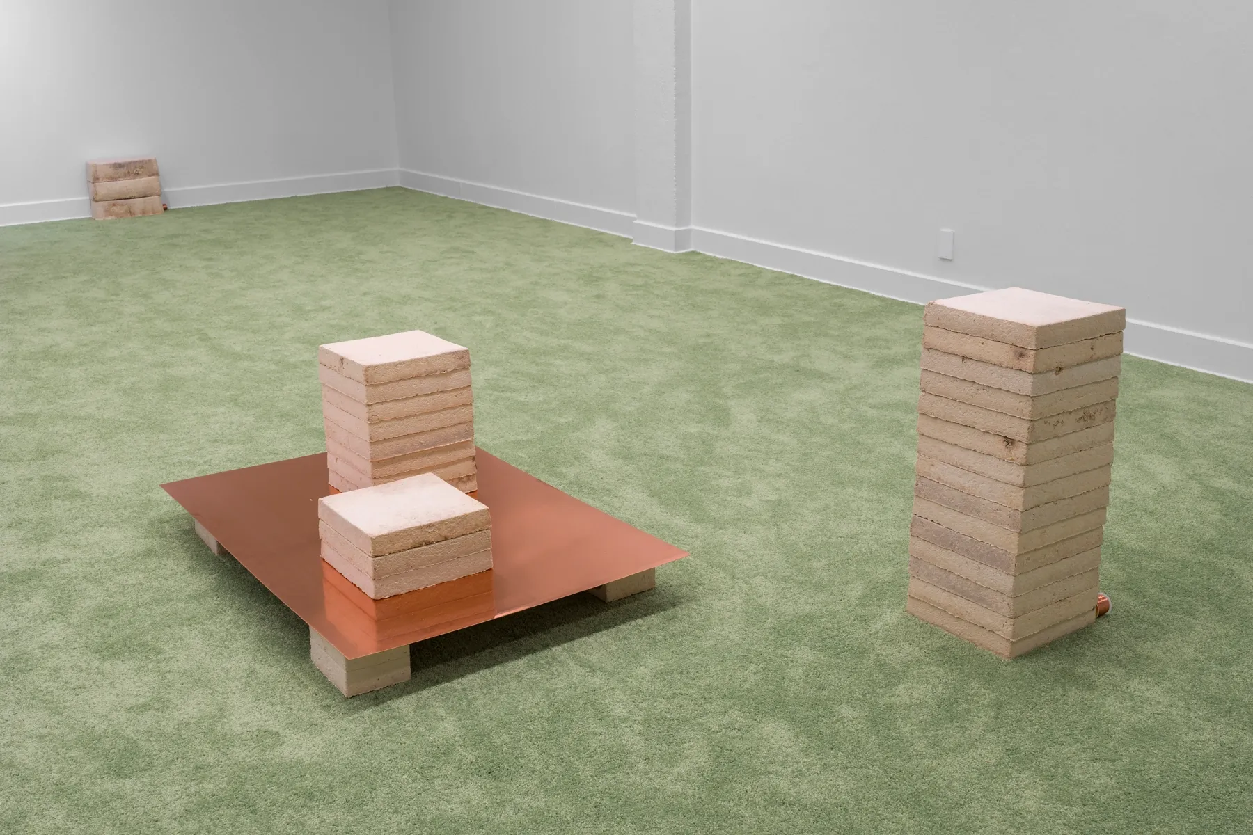 Patrick Bérubé at Plein Sud, Longueuil. Stacked mycelium blocks on a copper sheet and a freestanding column on green carpet.