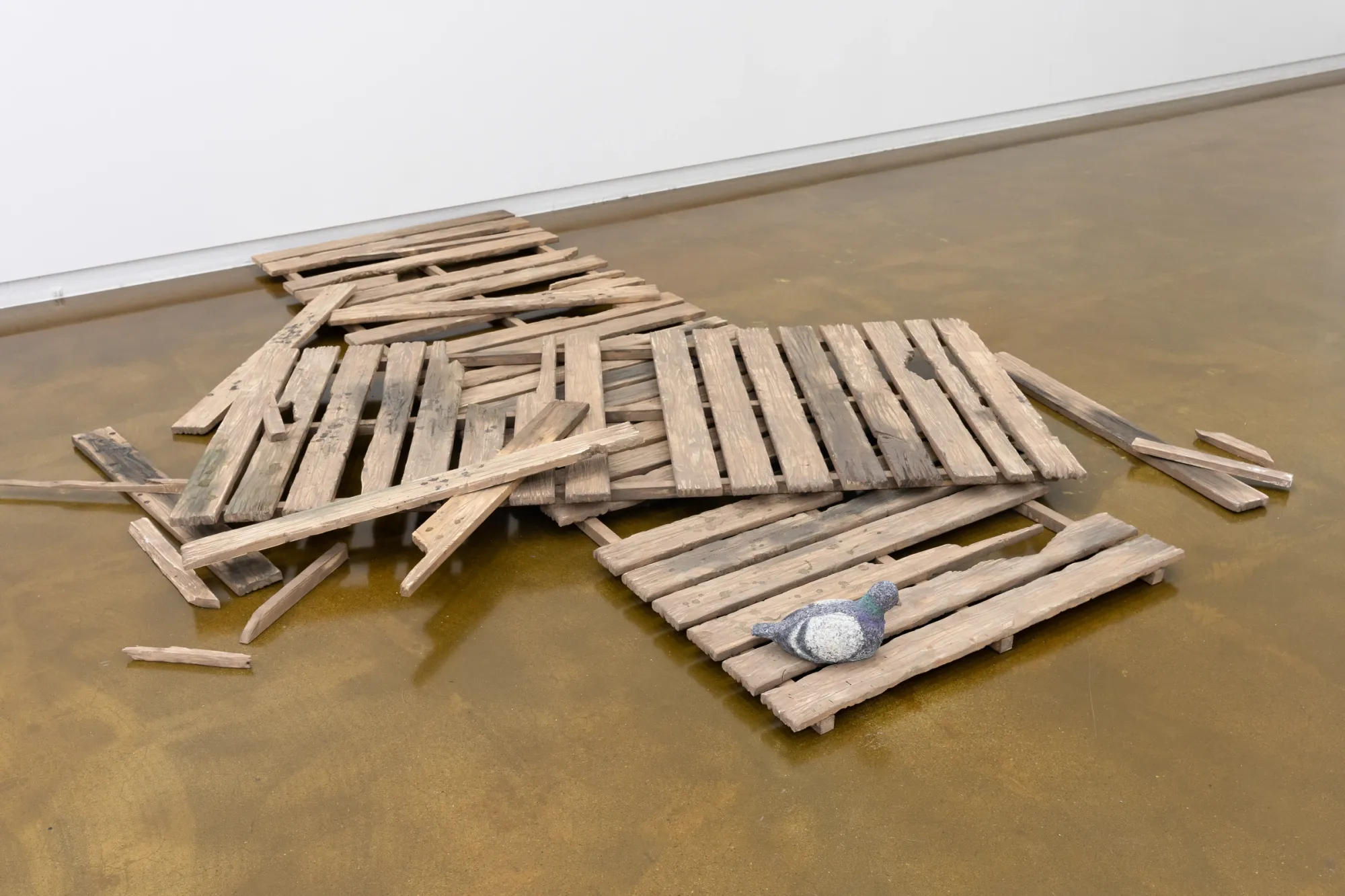 Seongeun Lee, Cheongju Art Studio, Cheongju: a small grey pigeon figure on a heap of weathered wood pallets and loose planks.