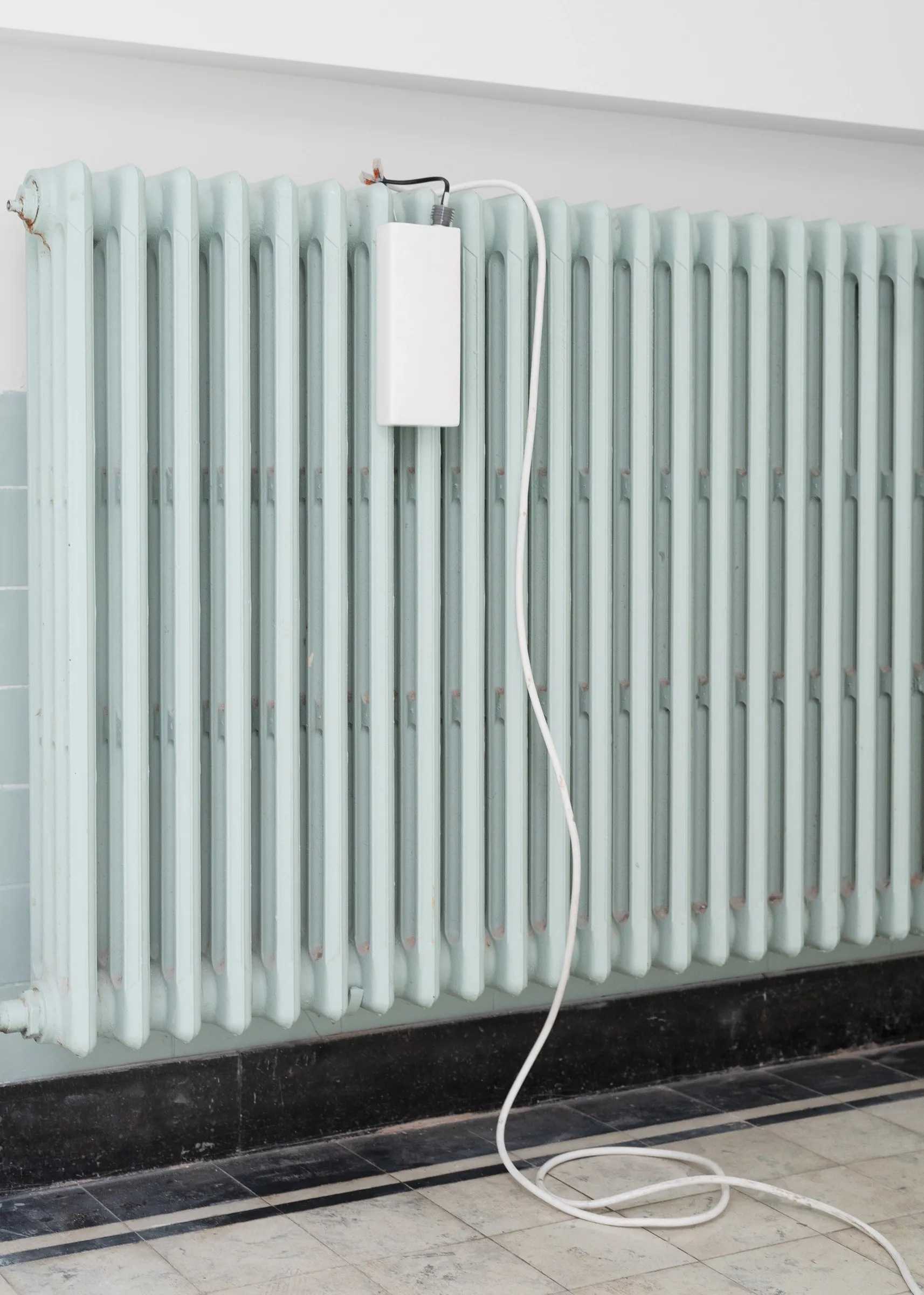 Exhibition review of Simon Bultynck: A. Aubry, A. Colin, P. Lippens, A. Oosterlinck, C. Wynants at CONVENT Space for Contemporary Art, Ghent, 2026. White box with a cable on a pale green radiator, the cable looping down to a tiled floor.