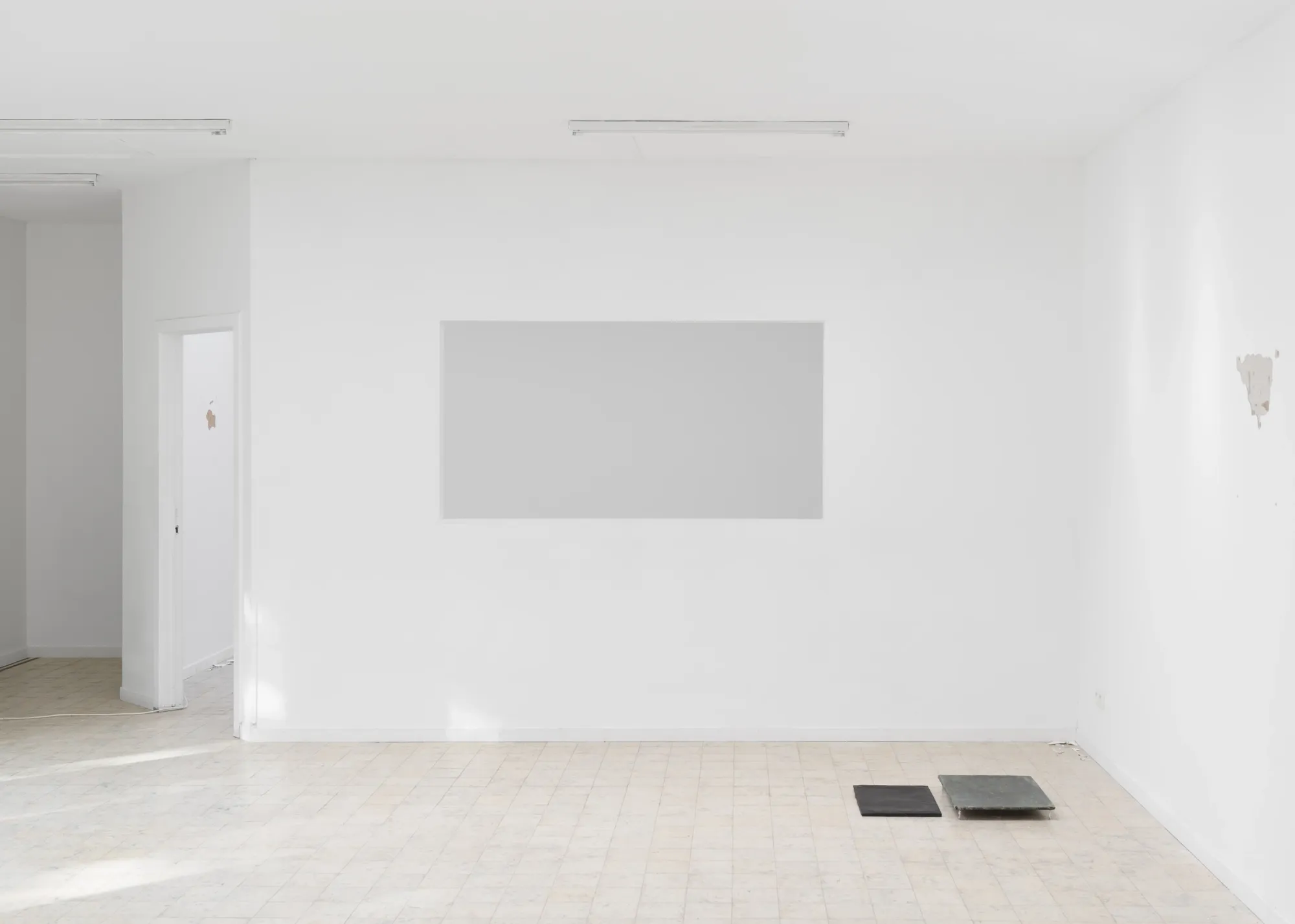 Exhibition review of Simon Bultynck: A. Aubry, A. Colin, P. Lippens, A. Oosterlinck, C. Wynants at CONVENT Space for Contemporary Art, Ghent, 2026. Two flat dark works on a tiled floor at the right of a white wall with a large rectangular opening.
