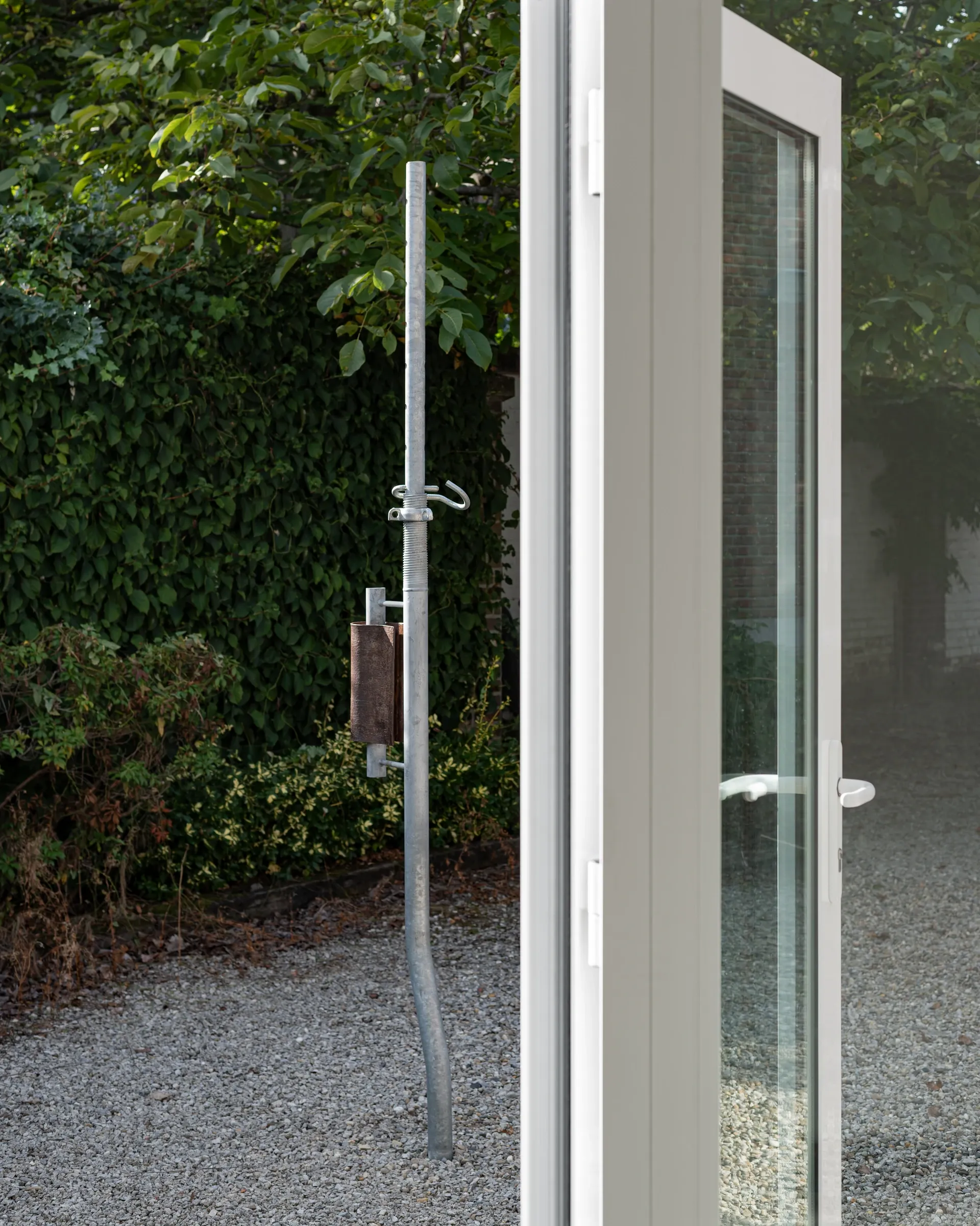 Exhibition review of Simon Bultynck: A. Aubry, A. Colin, P. Lippens, A. Oosterlinck, C. Wynants at CONVENT Space for Contemporary Art, Ghent, 2026. Galvanised steel prop with a hook and a rust-brown cylindrical form, seen through an open glass door in a gravel courtyard.