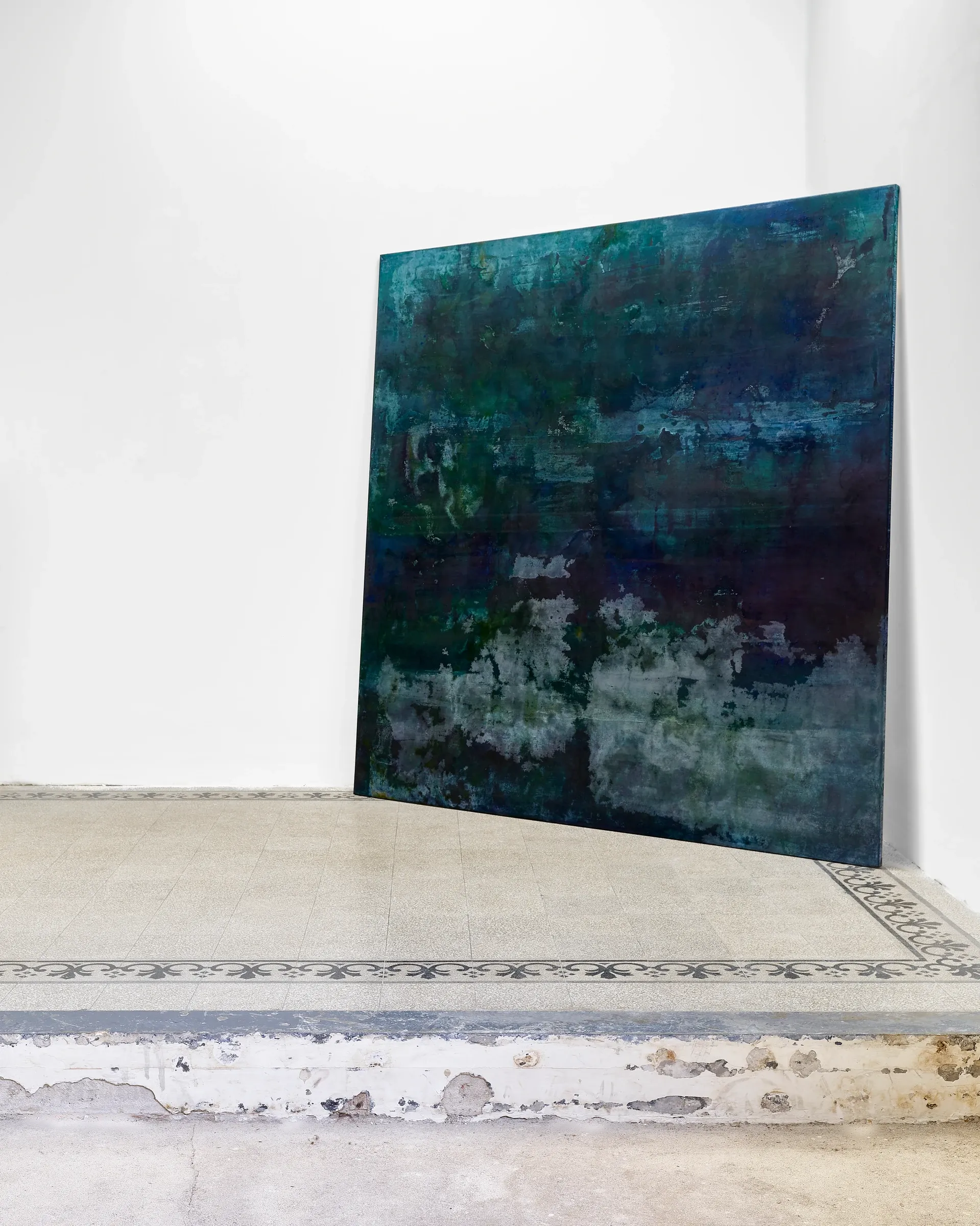 Taylah Hasaballah, INDICATRIX at The Address, Brescia, 2026. Blue-green painting leaning in a white corner above a stone floor.