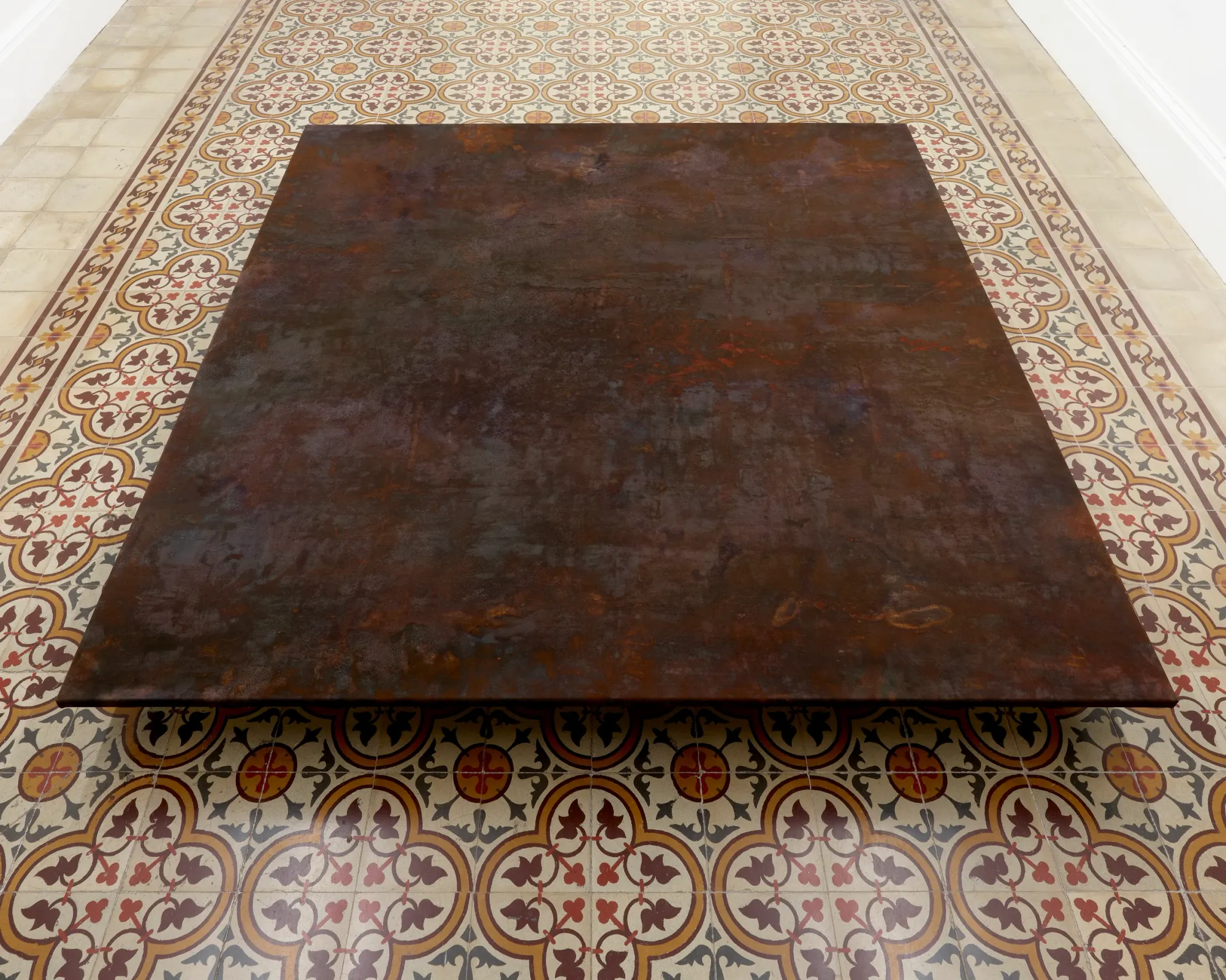 Taylah Hasaballah, INDICATRIX at The Address, Brescia, 2026. Large rust-brown floor panel seen from above on patterned tiles.