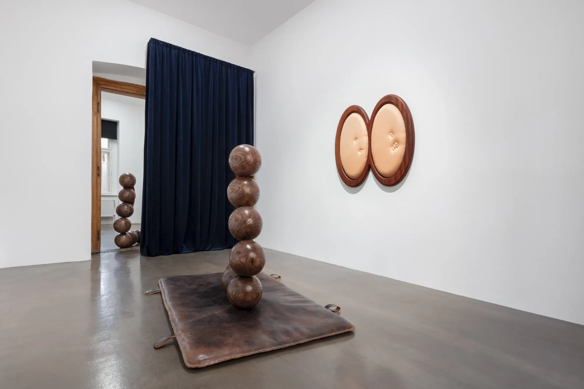 Tereza Kalousová, Clauda, Prague: stacked wooden spheres on a leather mat beside a peach double-oval wall work and a navy curtain