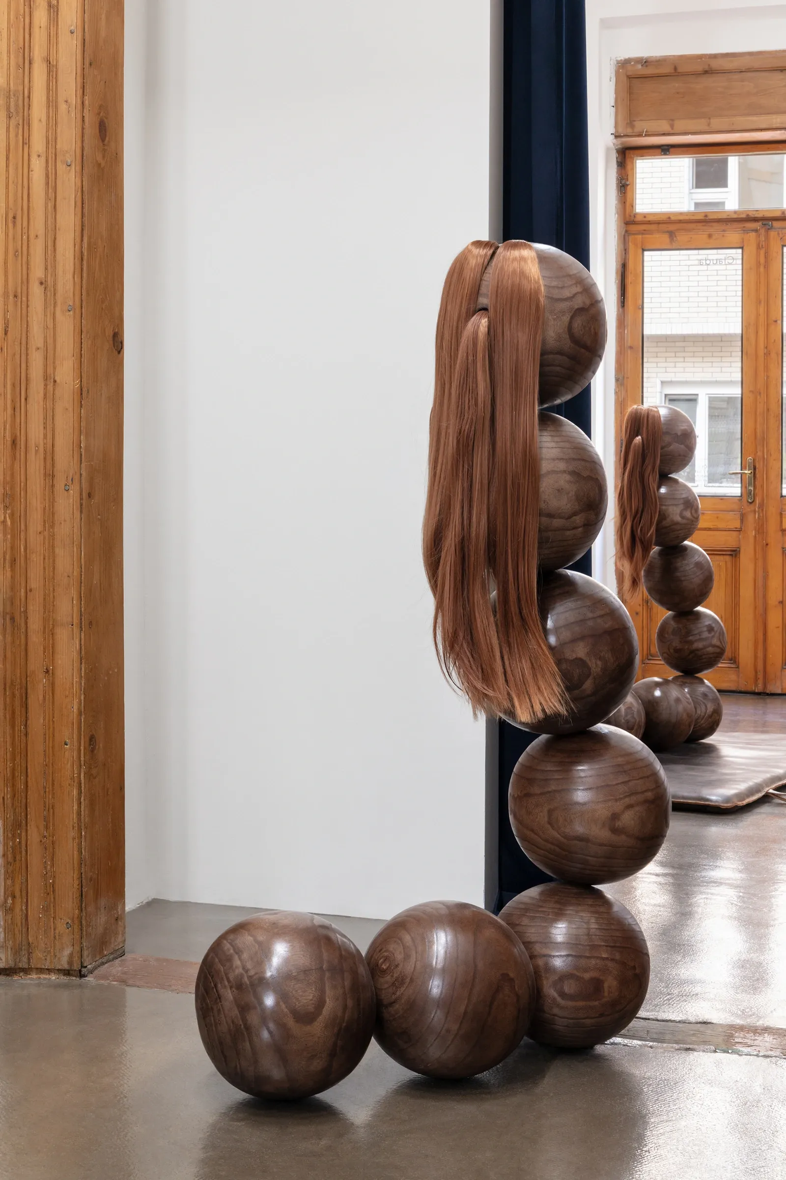 Tereza Kalousová, Clauda, Prague: wooden spheres with synthetic hair in two pigtails beside a wooden door frame.