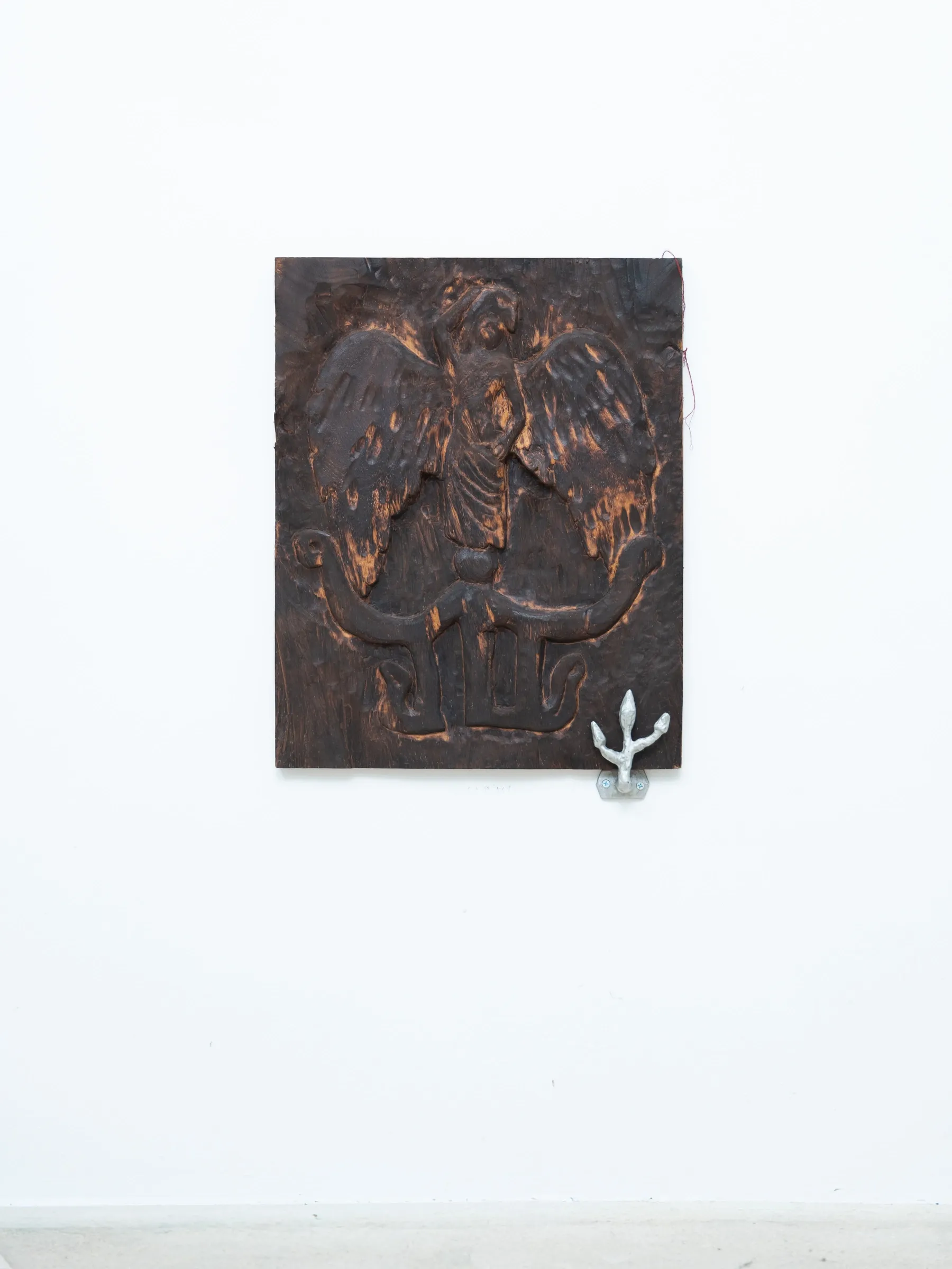 Yasy Bachurina, Studiya, Seoul: Charred wood relief of a winged figure on a white wall, with a small silver hook at lower right.