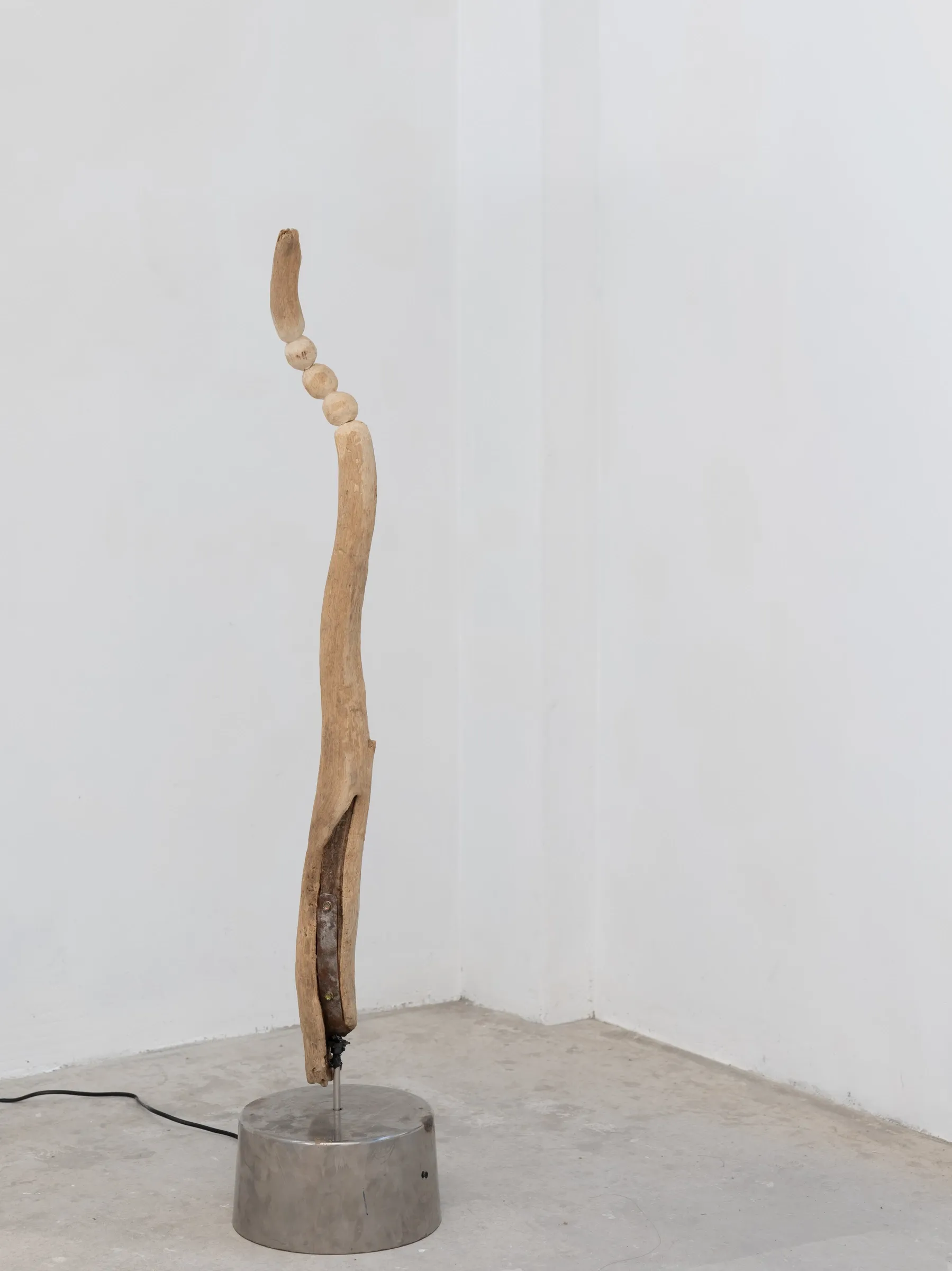 Yasy Bachurina, Studiya, Seoul: Tall split wooden pole on a metal base in a white corner, with a power cable on the floor.