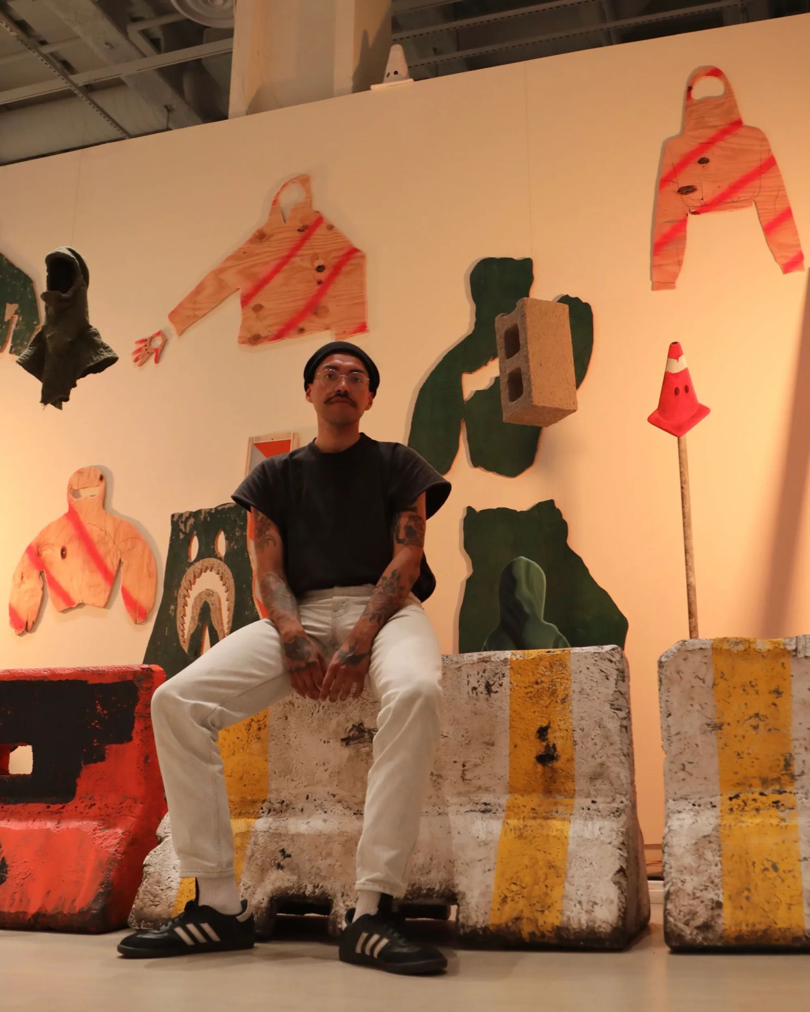 Daniel Castro portrait with installation view of hoodies and concrete sculptures, Bronx-born Puerto Rican artist exploring identity, humor, and authority in New York City.
