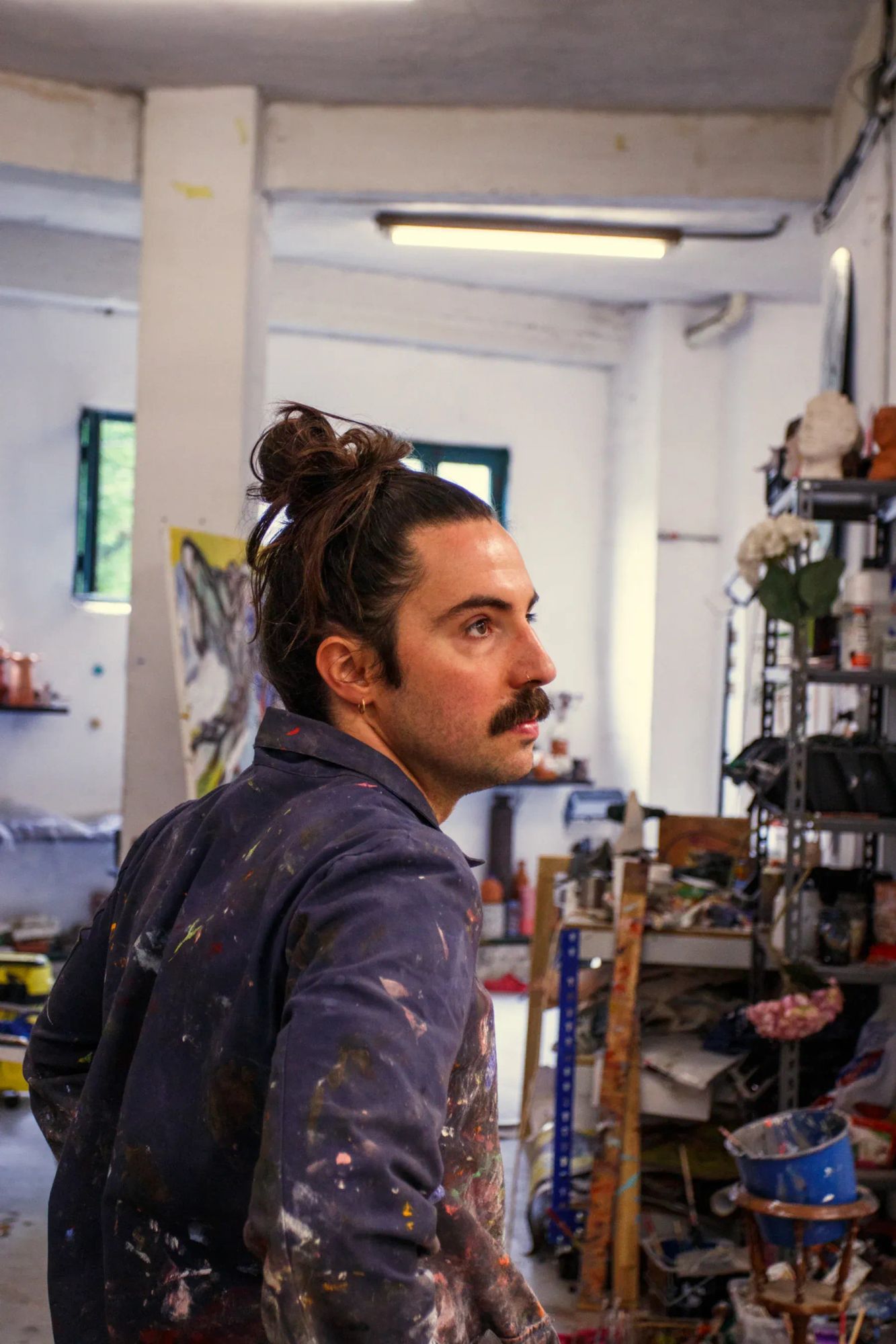 Manuel García Fernández, Spanish contemporary painter in his Oviedo studio, wearing a paint-splattered shirt, surrounded by tools and unfinished works.