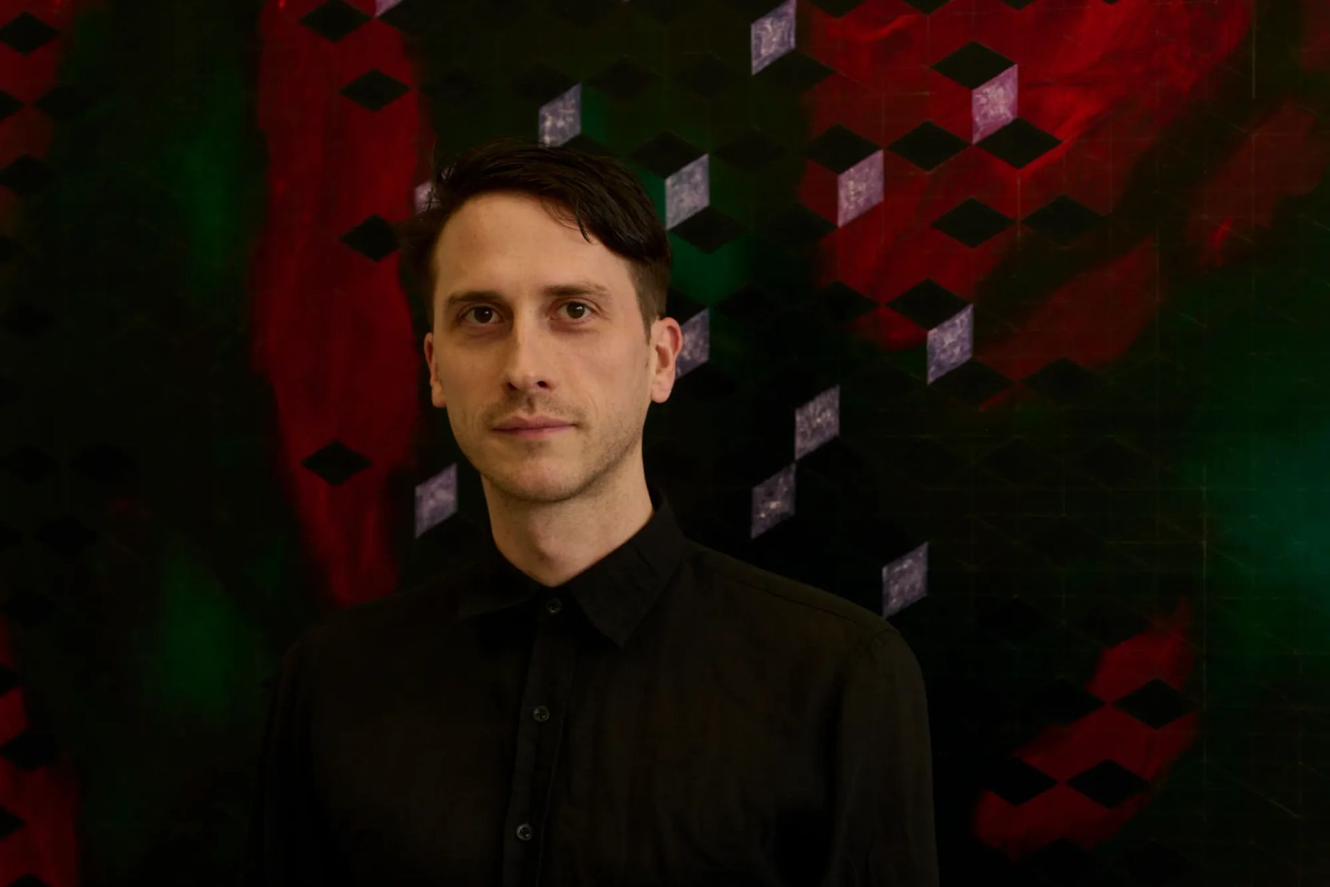 Matthias Esch, Berlin-based painter, portrait in front of a red-green geometric cube grid painting; contemporary abstraction about systems, structure and ornament; studio view.