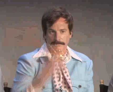 A man in a retro light-blue suit sits expressionless as glitter rains onto him, capturing the deadpan exhaustion and chaotic sparkle of December.