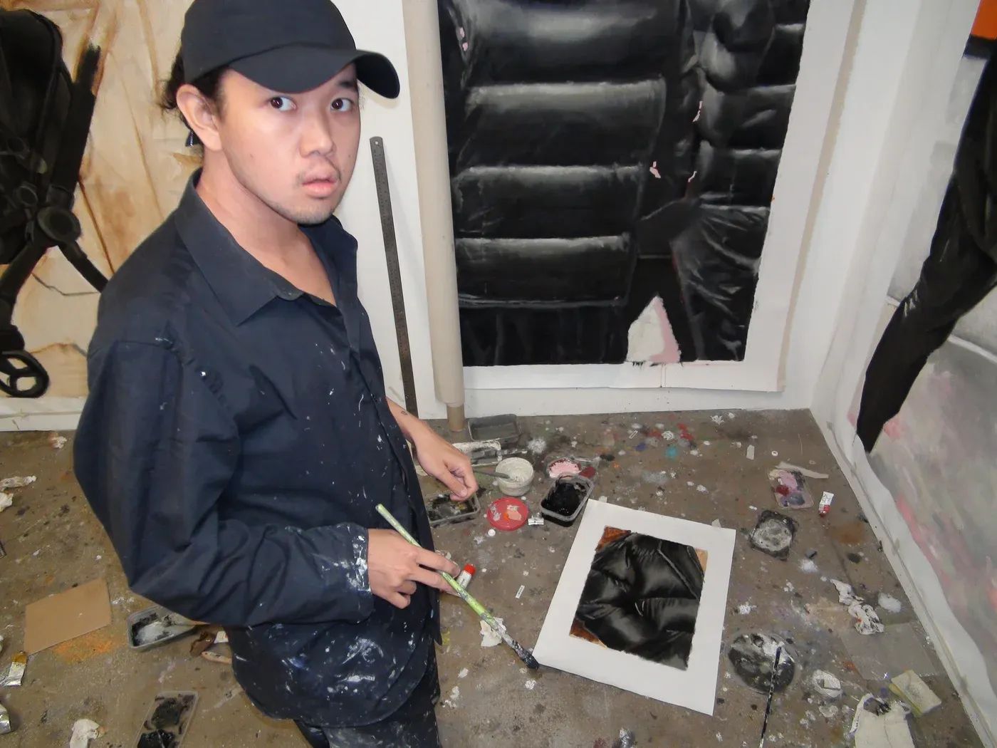 Artist Yutaro Inagaki holding a brush in his studio beside a large puffer jacket painting on the wall.