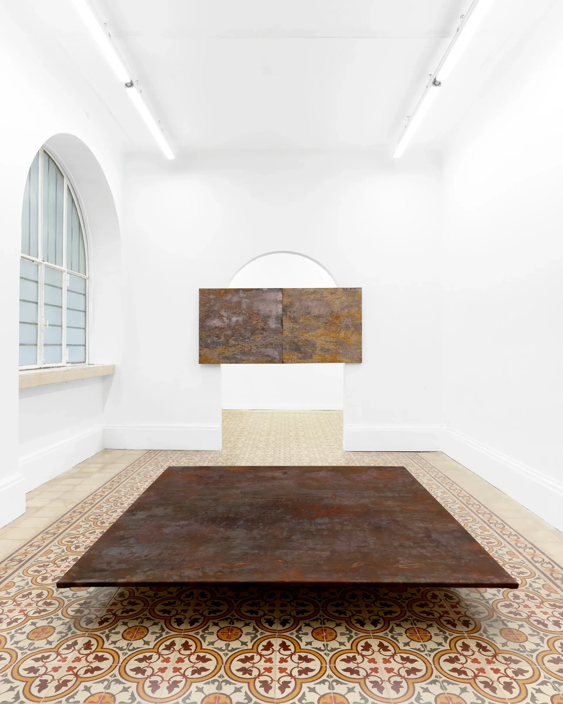 Taylah Hasaballah, INDICATRIX at The Address, Brescia, 2026. Rust-brown floor work with a two-panel painting behind.