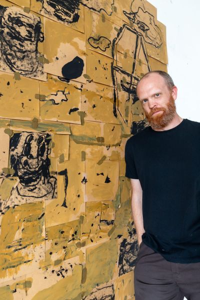 Portrait of contemporary artist Taylor Anton White standing in front of one of his large-format paper works: a yellow, collage-like composition