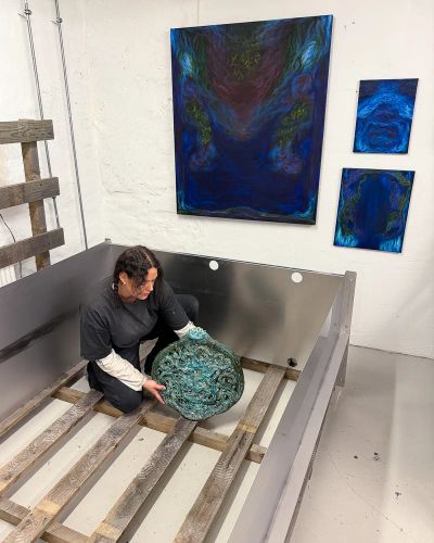 Artist Sofie Ehrhorn in her studio handling a glazed ceramic sculpture, surrounded by blue abstract paintings on the wall